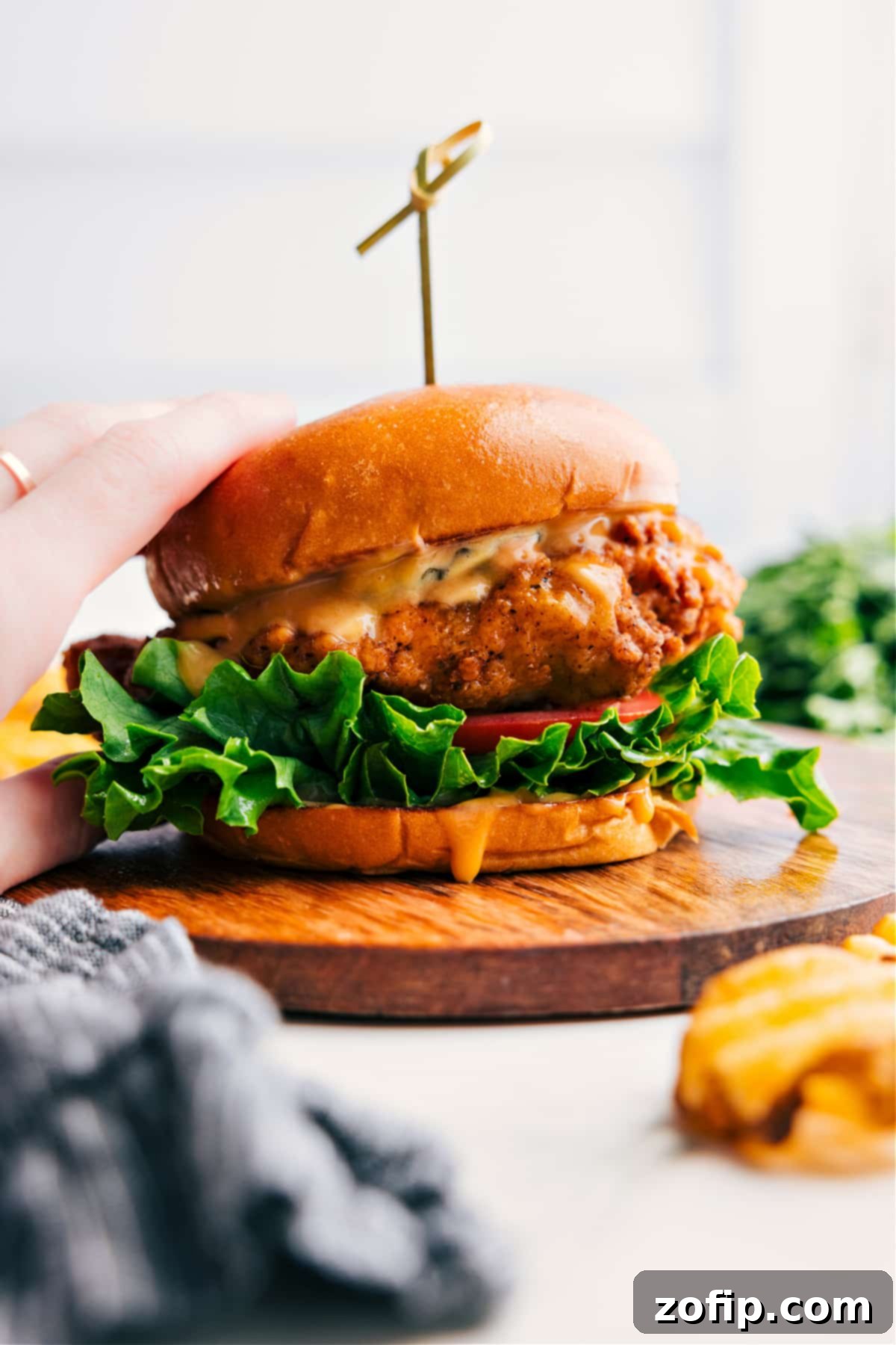 A mouthwatering crispy chicken sandwich on a toasted brioche bun with fresh lettuce, a slice of tomato, and a creamy, flavorful sauce.