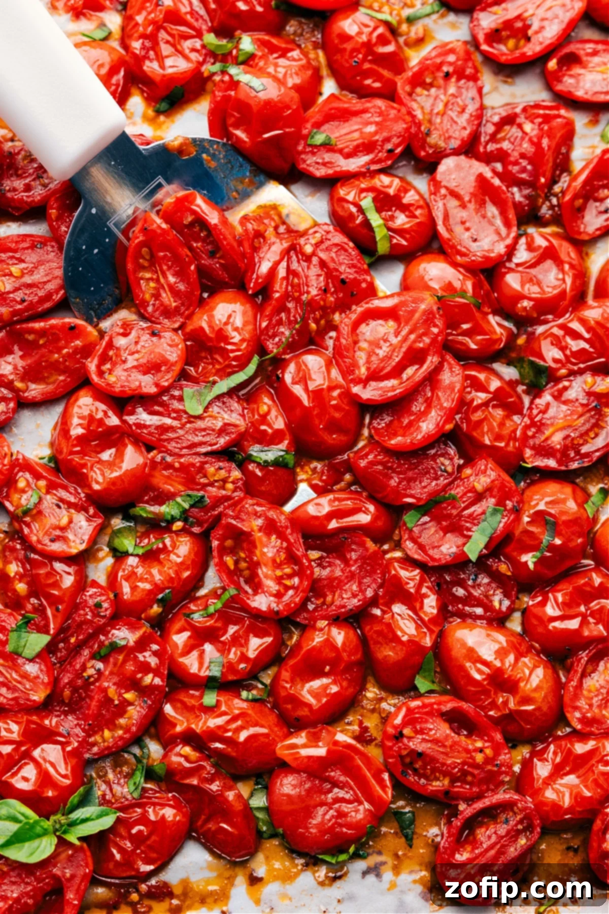 Simple And Delicious Roasted Cherry Tomatoes Recipe Perfectly roasted cherry tomatoes on a sheet pan, with a spatula lifting a portion to show their juicy, caramelized texture.