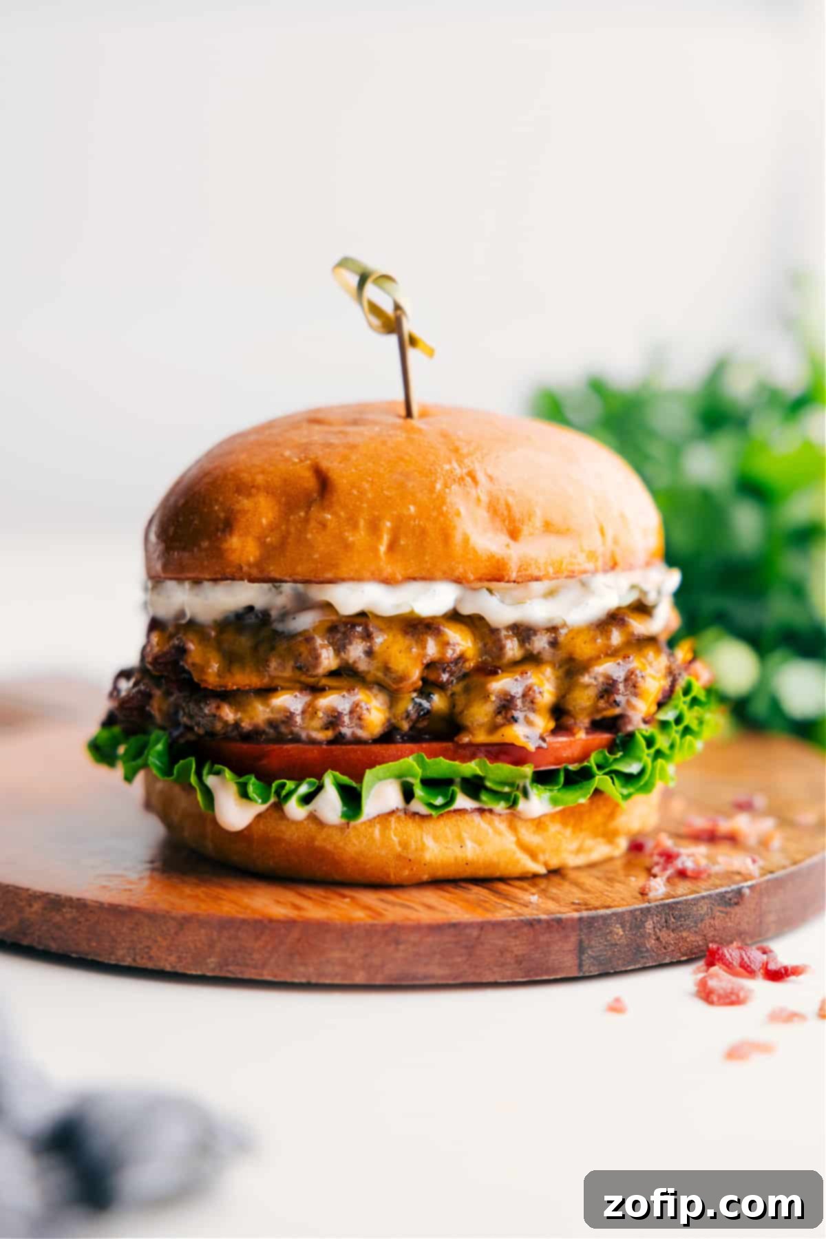 A delicious Crack Burger on a plate with melted cheese, fresh tomato, crisp lettuce, and a generous drizzle of creamy crack sauce.