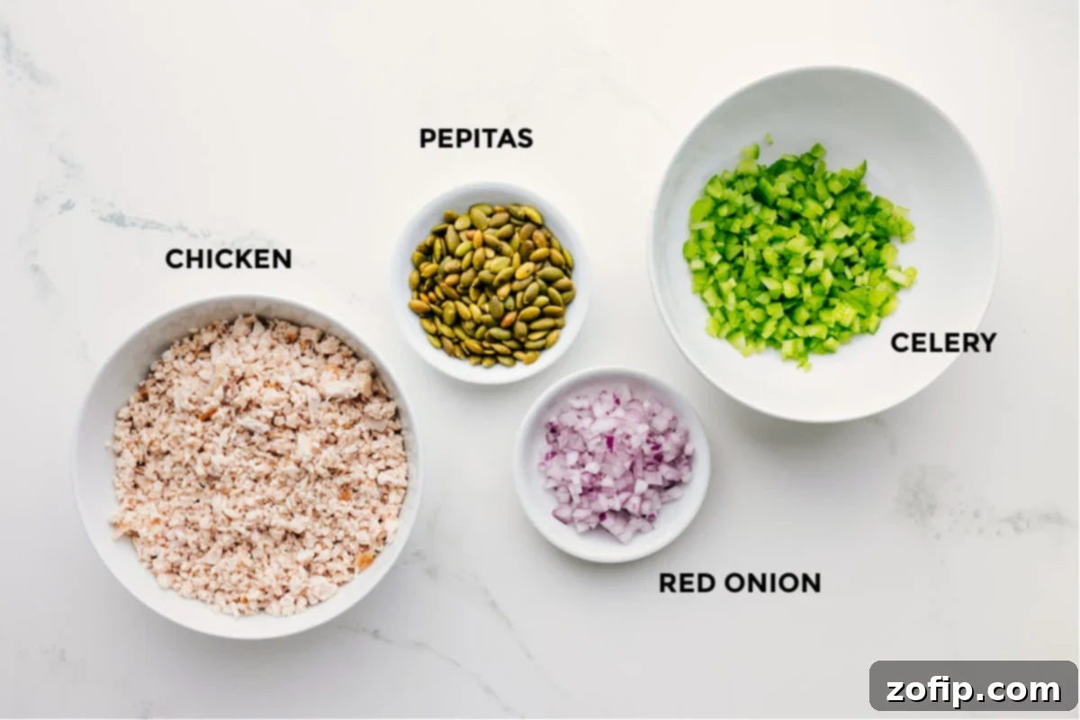 Fresh ingredients laid out for Green Goddess Chicken Salad, including shredded chicken, diced celery, red onion, and roasted pepitas.