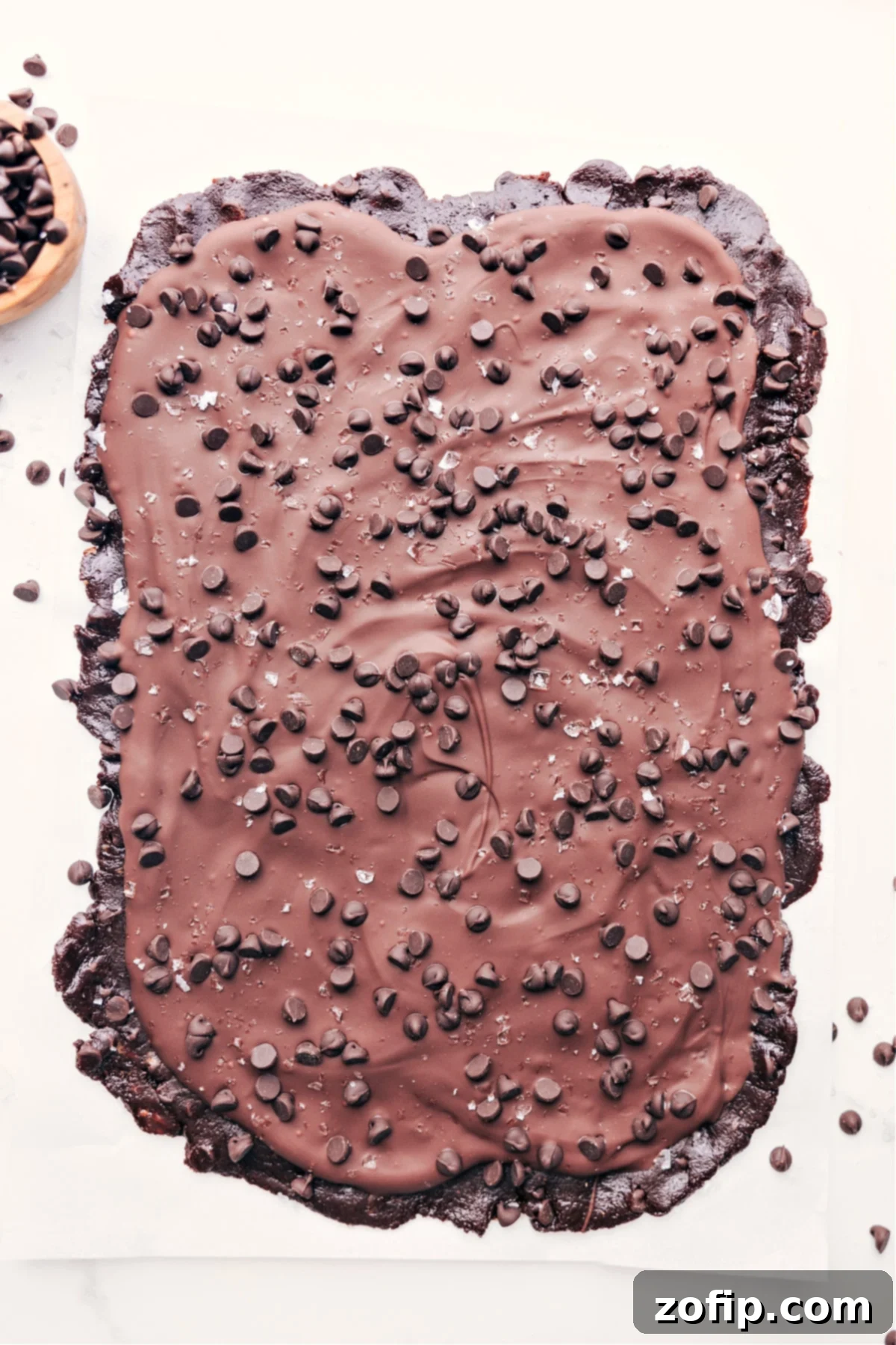 Healthy brownie batter bark with a thick layer of melted chocolate on top with more chocolate chips, ready to be broken into pieces.