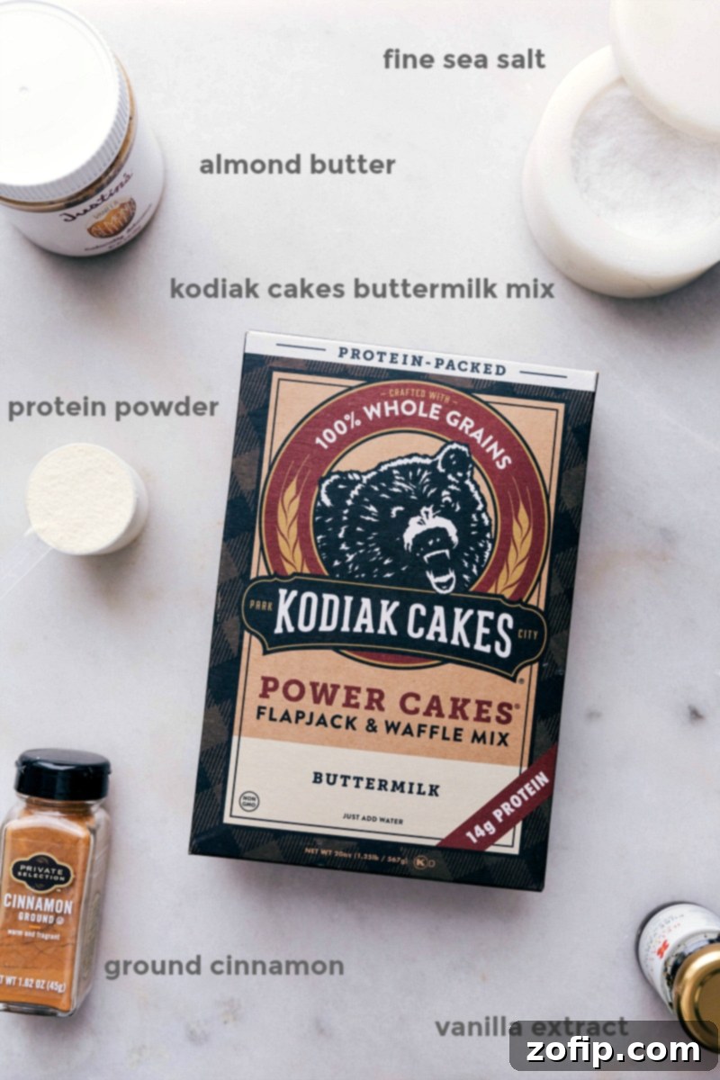 Assortment of fresh ingredients for the high protein breakfast cookies, including Kodiak Cakes buttermilk mix, almond butter, maple syrup, vanilla protein powder, and cinnamon, neatly arranged on a counter.