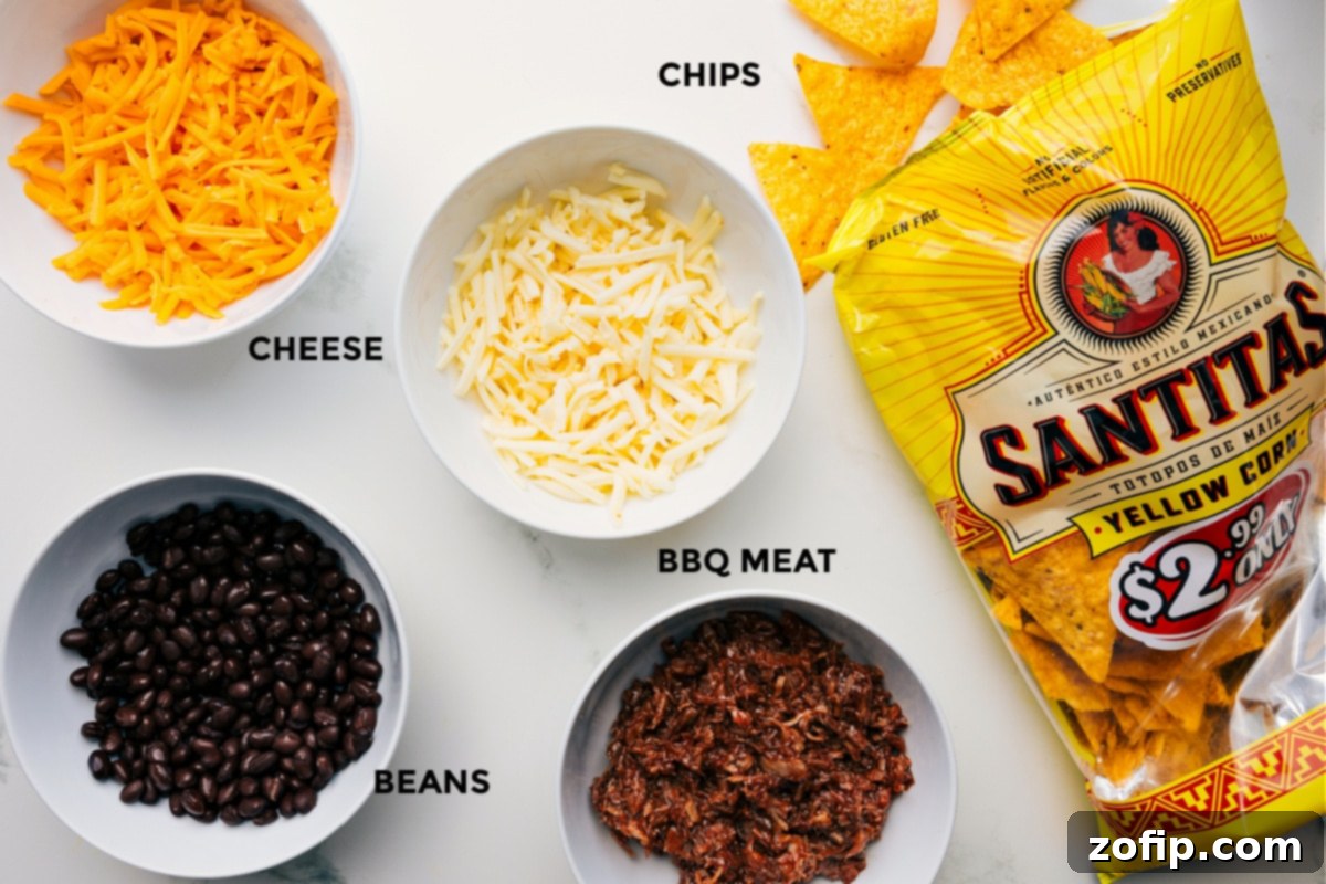 Ingredients for Pulled Pork Nachos are neatly prepped and laid out on a kitchen counter, including shredded cheeses, black beans, pulled pork, and a pile of tortilla chips.