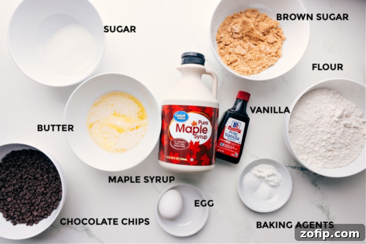 All the essential ingredients for Tiny Chocolate Chip Cookies, meticulously prepped and ready for assembly: unsalted butter, both light brown and granulated sugars, a large egg, pure vanilla extract, a bottle of pure maple syrup, cornstarch, salt, baking soda, baking powder, all-purpose flour, and a generous bowl of mini chocolate chips.