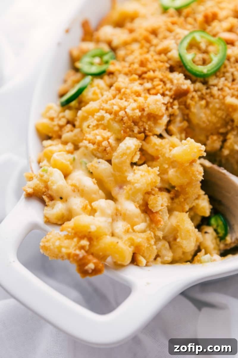 A serving of Jalapeño Popper Mac & Cheese being scooped from a baking dish, showcasing its gooey cheese, crispy topping, and visible pieces of jalapeño and bacon.