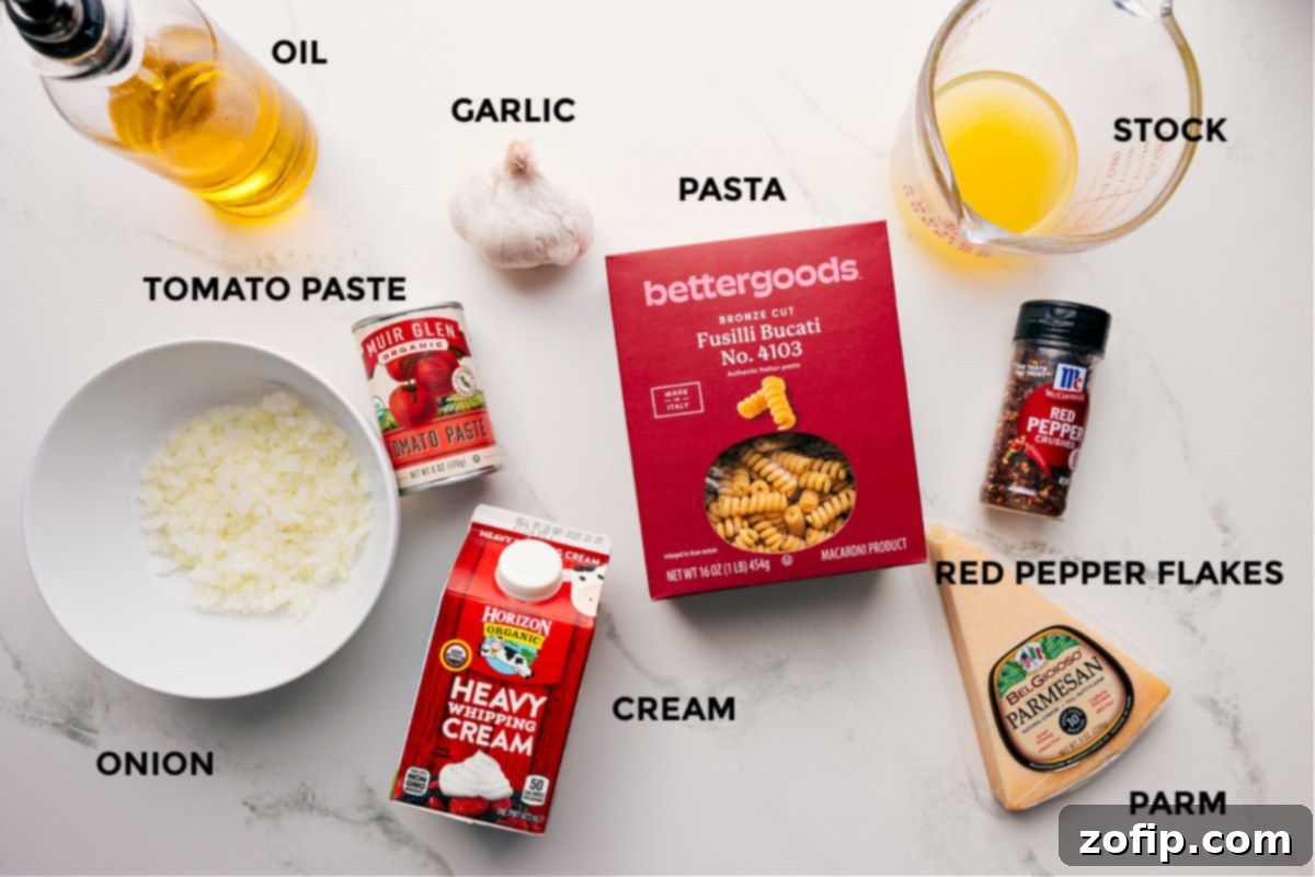 A collection of fresh ingredients for creamy tomato pasta, including olive oil, finely diced onion, minced garlic, tomato paste, heavy cream, chicken stock, red pepper flakes, dried pasta, and a block of Parmesan cheese.