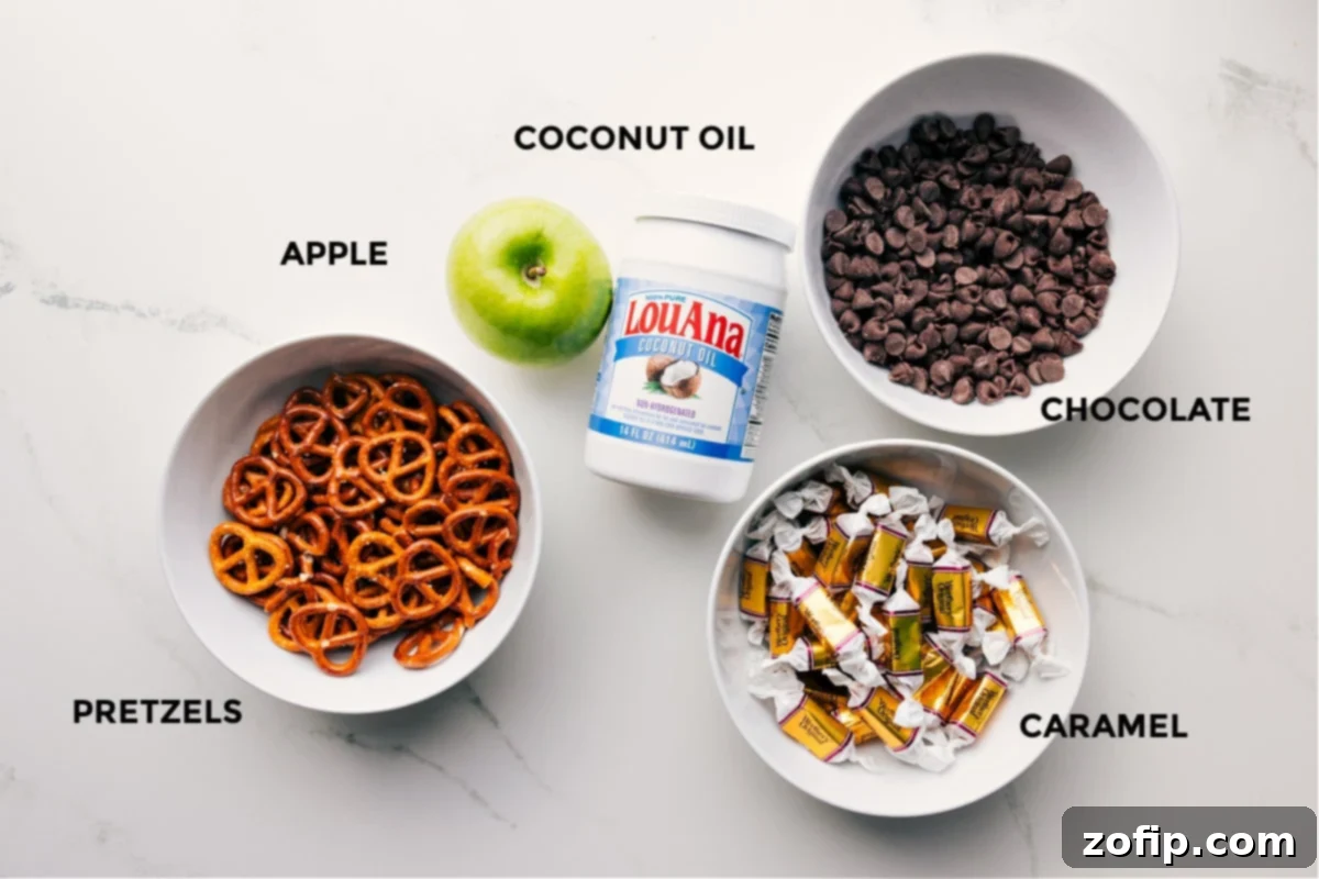 Ingredients for Caramel Apple Bark prepped and laid out, including mini pretzels, diced Granny Smith apple, chocolate chips, coconut oil, soft caramels, and heavy cream.