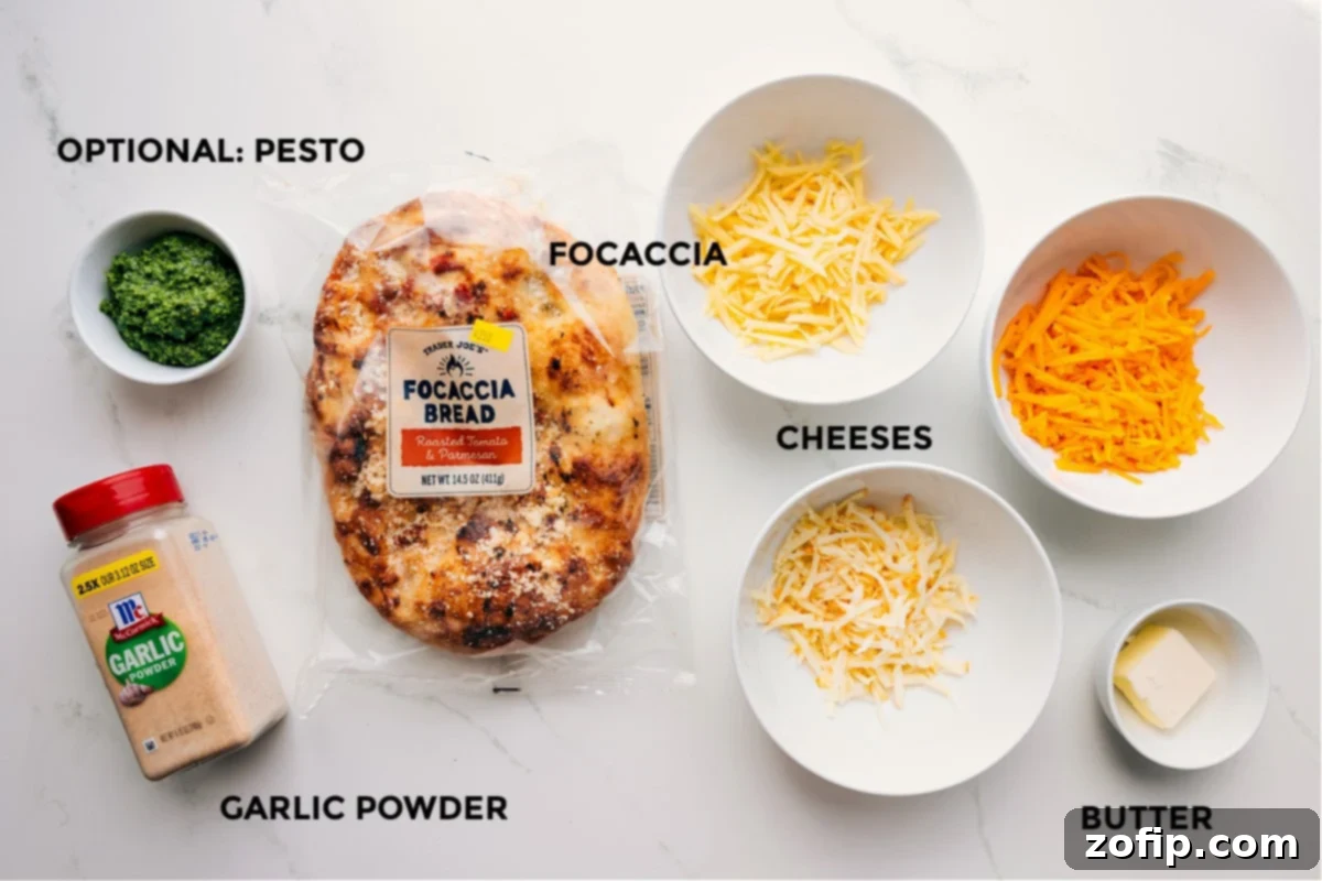 Key ingredients for Focaccia Grilled Cheese laid out neatly: focaccia bread, various cheeses, softened butter, garlic powder, salt, and a small dish of pesto.