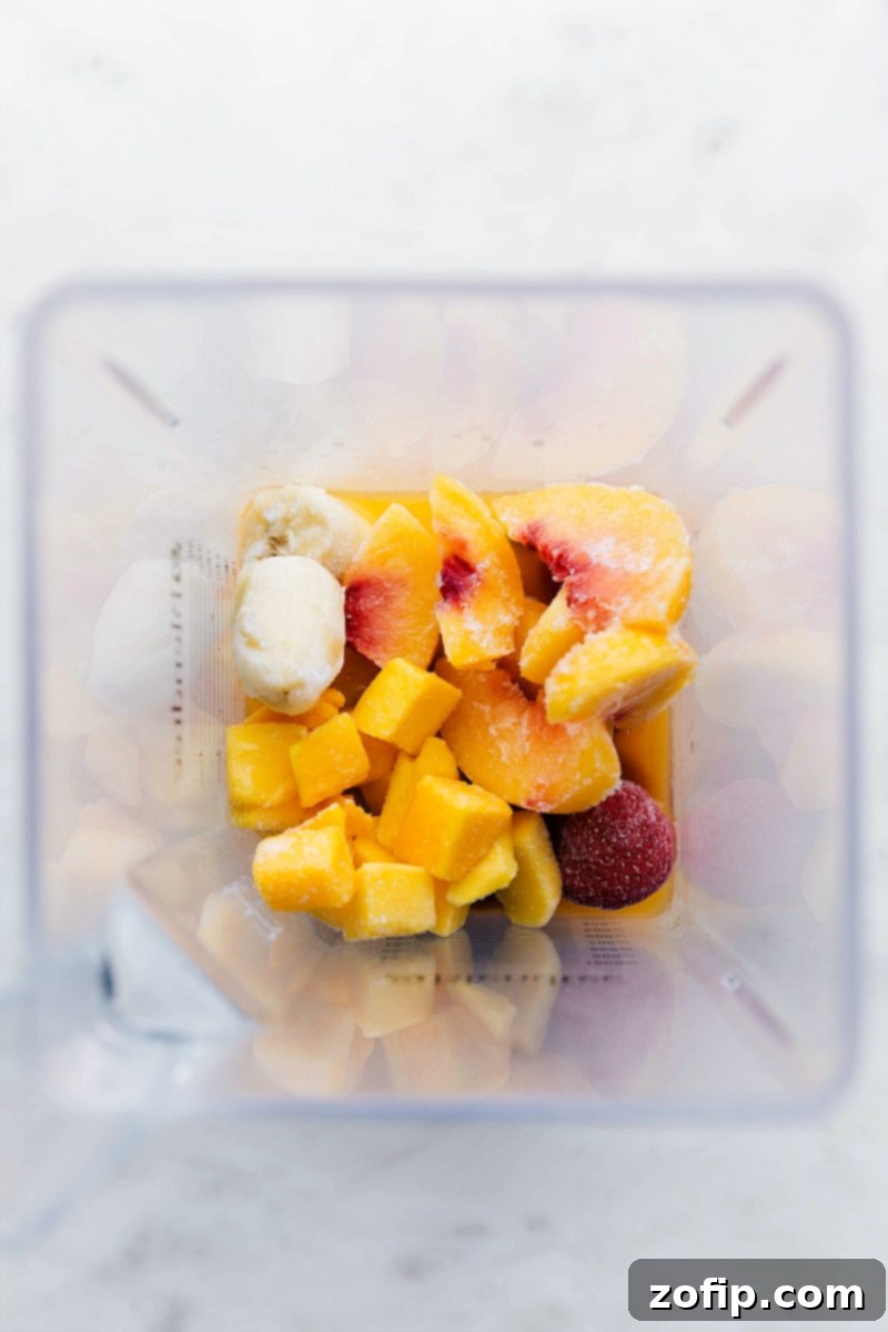 All the vibrant, frozen fruit ingredients, including mango, strawberries, peaches, and banana, carefully placed into a blender, ready for blending into a delicious smoothie.
