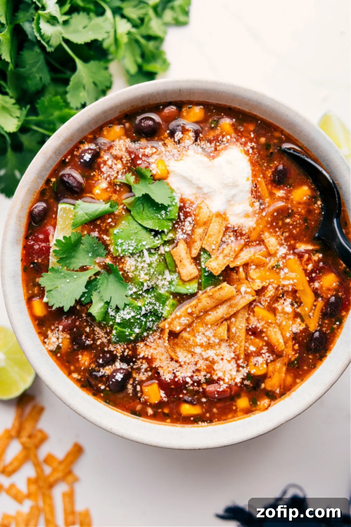 A bowl of hot Chicken Taco Soup loaded with all the best toppings: fresh cilantro, crispy tortilla strips, a dollop of sour cream, and a sprinkle of shredded cheese.