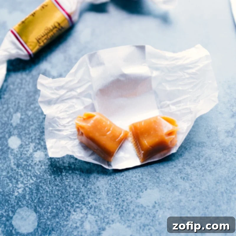 A close-up process shot of a soft caramel candy being cut in half, ready to be stuffed into cookie dough.