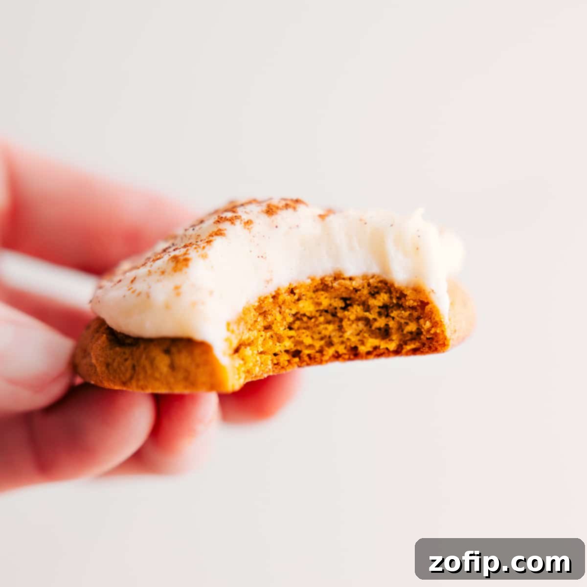 Best Pumpkin Cookies Topped With Cream Cheese Frosting A perfectly soft pumpkin cookie topped with generous cream cheese frosting, with a bite taken out, showcasing its delightful texture.