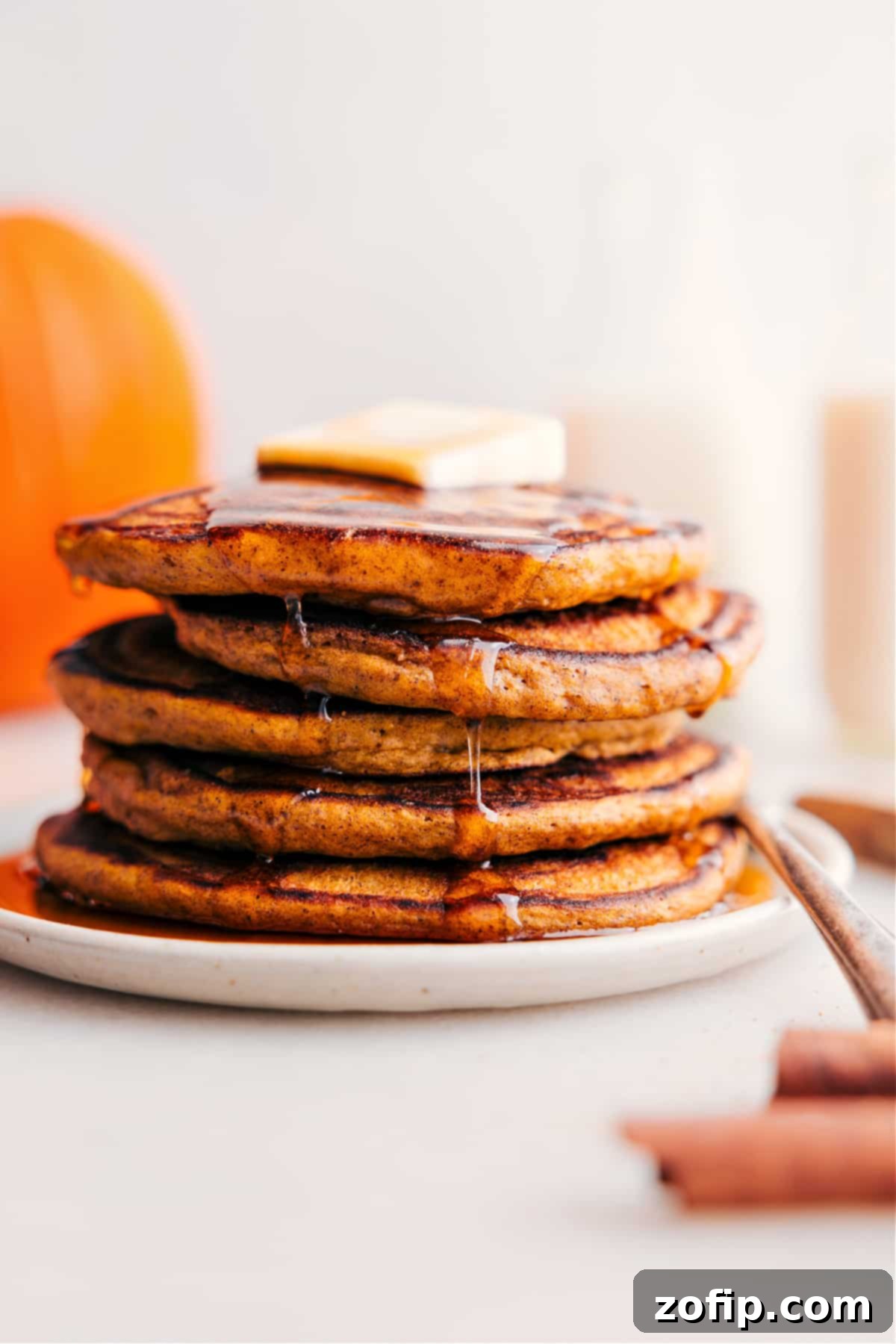 Start Your Fall Mornings with the Best Pumpkin Pancakes A towering stack of perfectly fluffy pumpkin pancakes, generously topped with a pat of butter and drizzled with warm maple syrup, ideal for a fall breakfast.