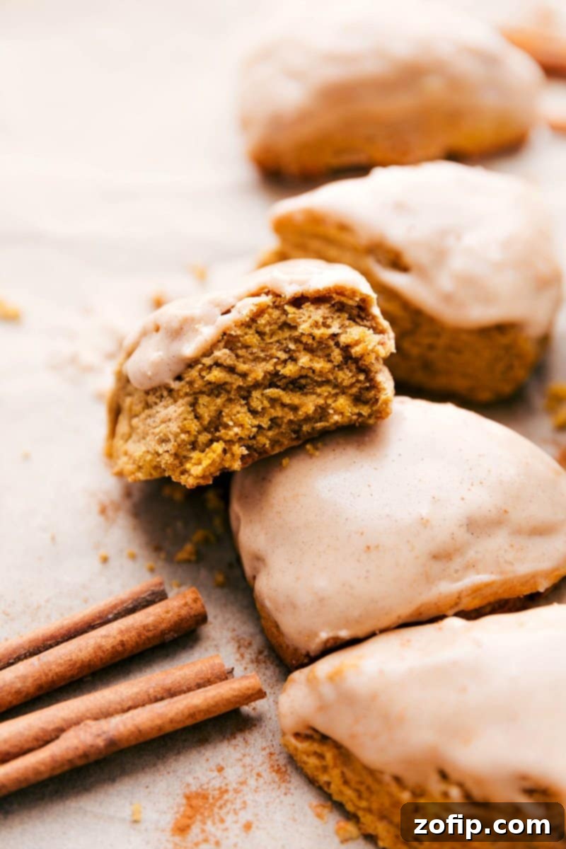 Pumpkin Scones with a Sweet Pumpkin Glaze Recipe Delightful pumpkin scones, generously drizzled with a sweet glaze, with one scone showing a bite taken out to reveal its soft interior.