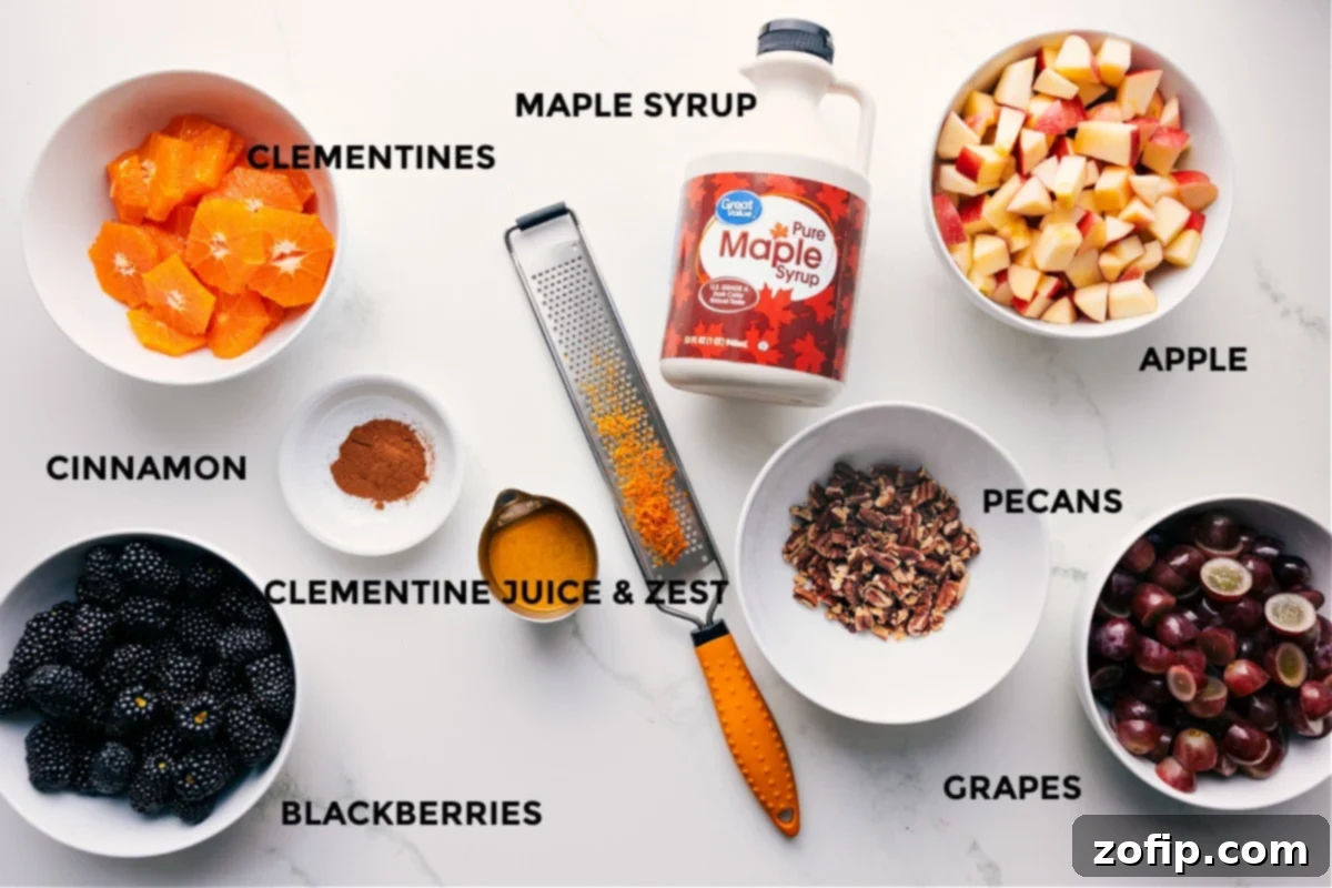 All the ingredients for Fall Fruit Salad prepped for easy assembly, including clementines, blackberries, grapes, apples, pecans, cinnamon, orange juice and zest, and maple syrup.