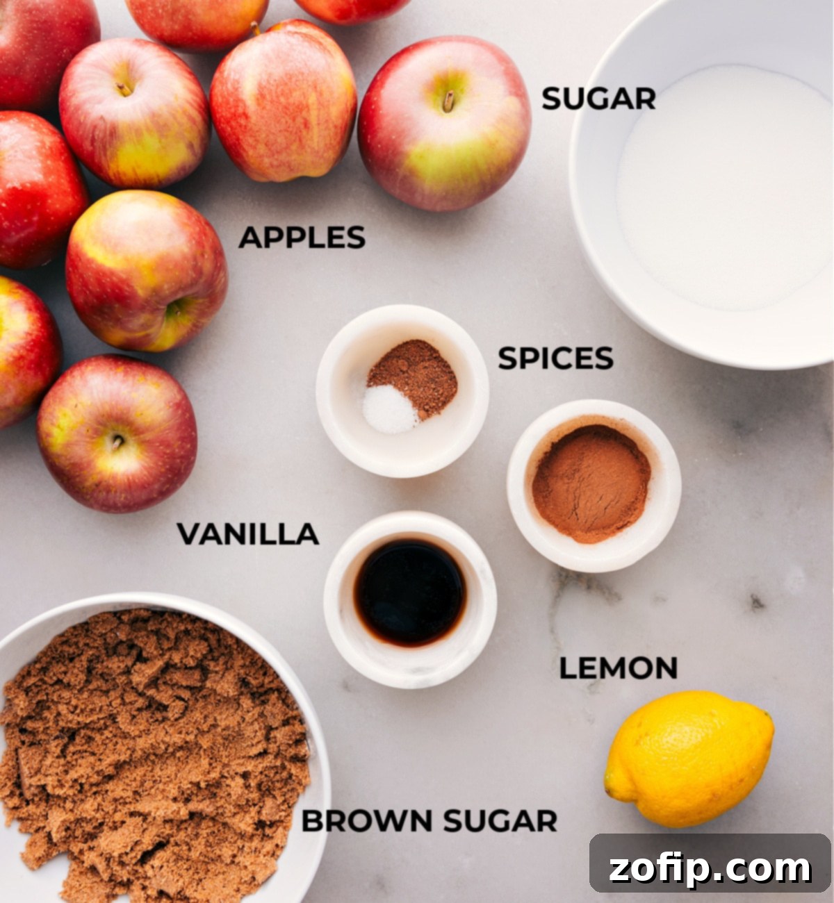 Assorted ingredients for slow cooker apple butter laid out, including fresh apples, cinnamon sticks, ground nutmeg, vanilla extract, brown sugar, and granulated sugar.
