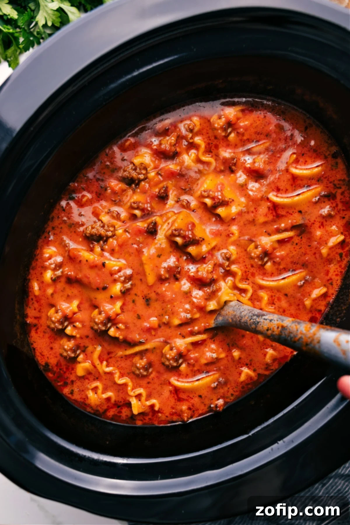 Crockpot Lasagna Soup in a slow cooker with a large scoop being lifted out, showcasing rich broth, pasta, and meat.