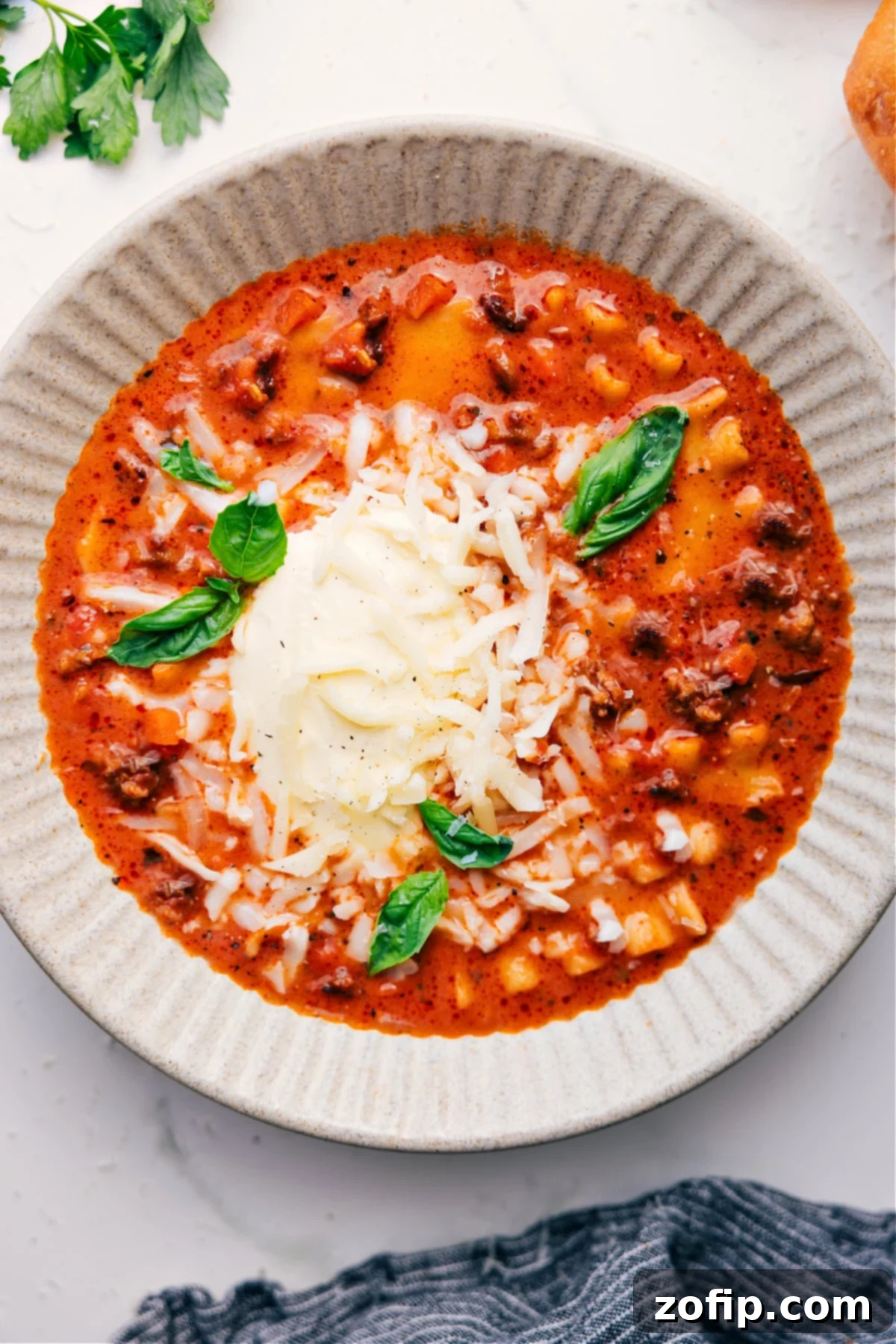 A beautifully presented bowl of Crockpot Lasagna Soup, topped with freshly grated cheese and vibrant basil leaves, steaming and ready to be enjoyed as the perfect comfort food meal.
