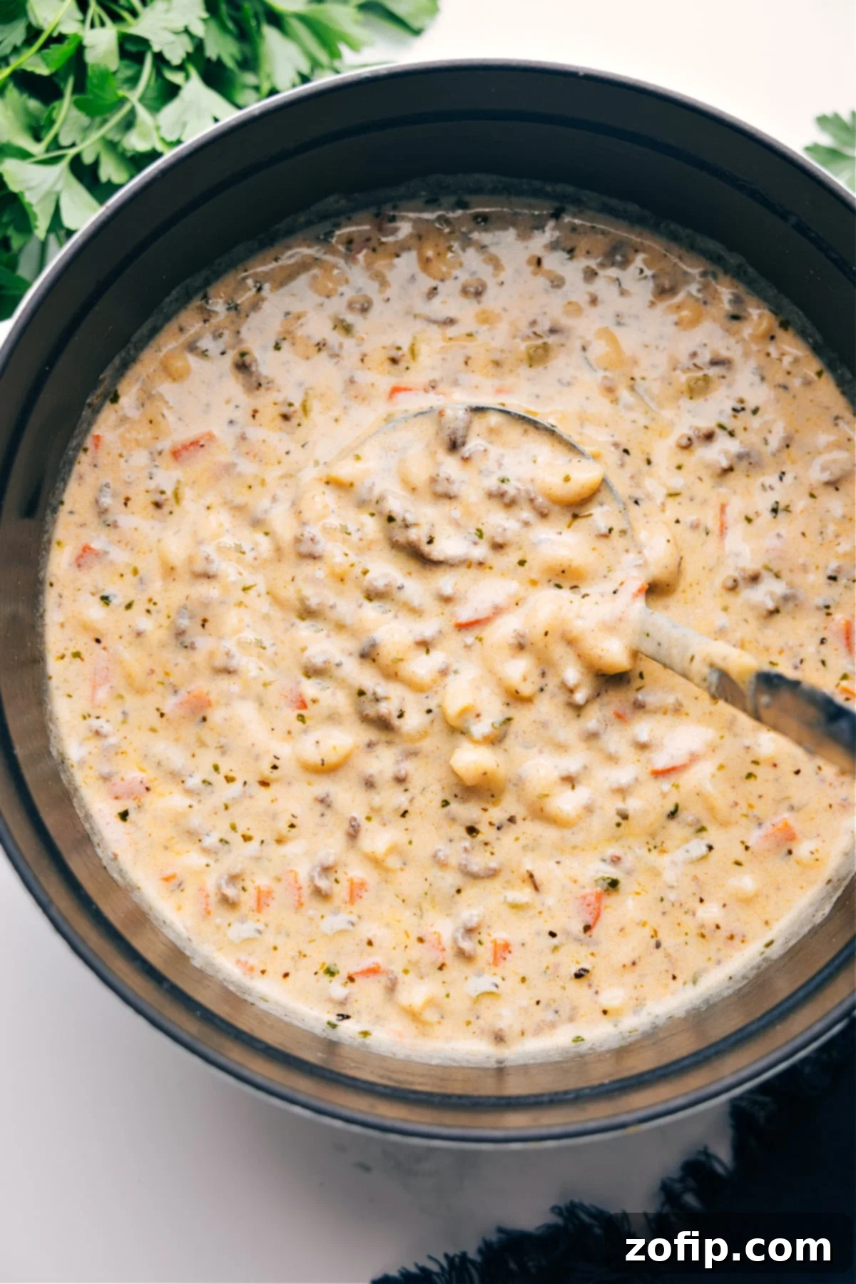 A large pot filled with bubbling Cheeseburger Macaroni Soup, featuring visible pieces of ground beef, tender elbow macaroni, and a rich orange-yellow cheesy broth, garnished with fresh parsley and ready to be served.