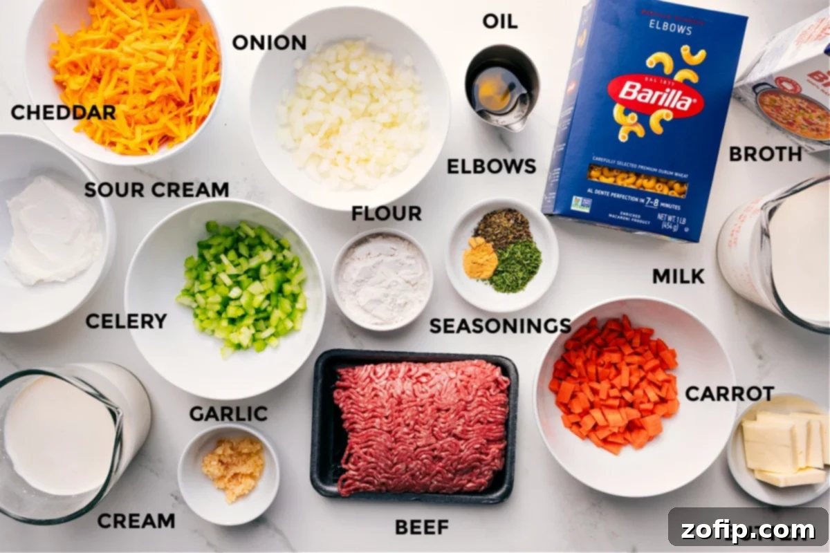 A vibrant flat lay of all fresh ingredients for Cheeseburger Macaroni Soup: a container of sour cream, a small pitcher of heavy cream, a block of freshly shredded sharp cheddar cheese, finely diced onion, sliced celery, minced garlic cloves, all-purpose flour, a package of lean ground beef, various dried seasonings (basil, parsley, ground mustard, salt, pepper), a bottle of olive oil, diced carrots, a pitcher of whole milk, a stick of butter, uncooked elbow pasta, and a carton of chicken broth.