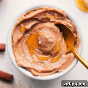 A bowl of creamy, homemade Honey Butter, drizzled with extra honey, sits on a rustic wooden board, ready to be served. It's garnished with a sprinkle of flaky sea salt, enhancing its visual appeal.