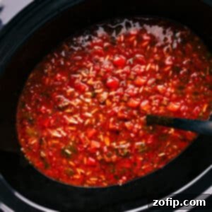 Hearty Crockpot Stuffed Pepper Soup served in a white bowl, garnished with fresh parsley and shredded cheese, with a spoon ready.