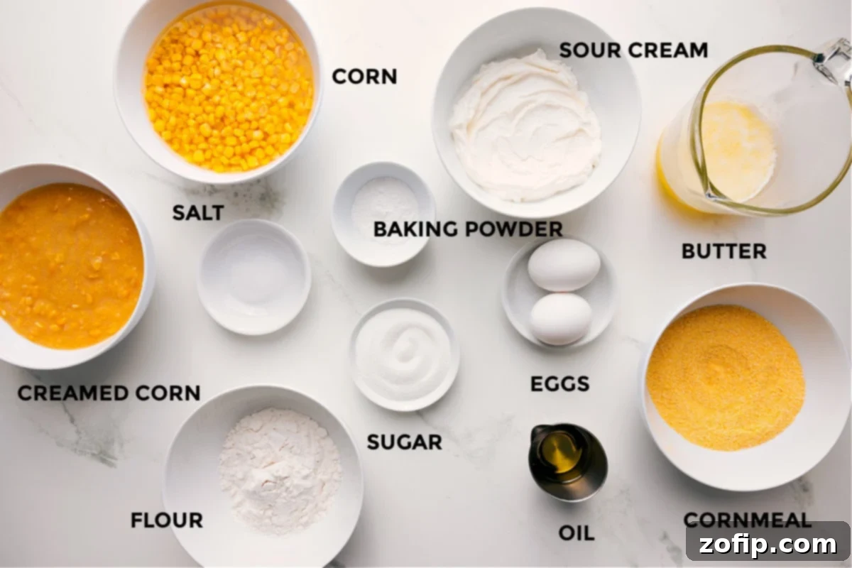 All the ingredients in this recipe prepped out for easy assembly including the creamed corn, corn, salt, flour, baking powder, sugar, sour cream, eggs, oil, cornmeal, and butter.