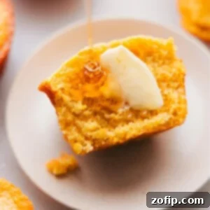 Freshly baked cornbread muffin, cut in half to reveal its fluffy interior, served with butter and honey on top.