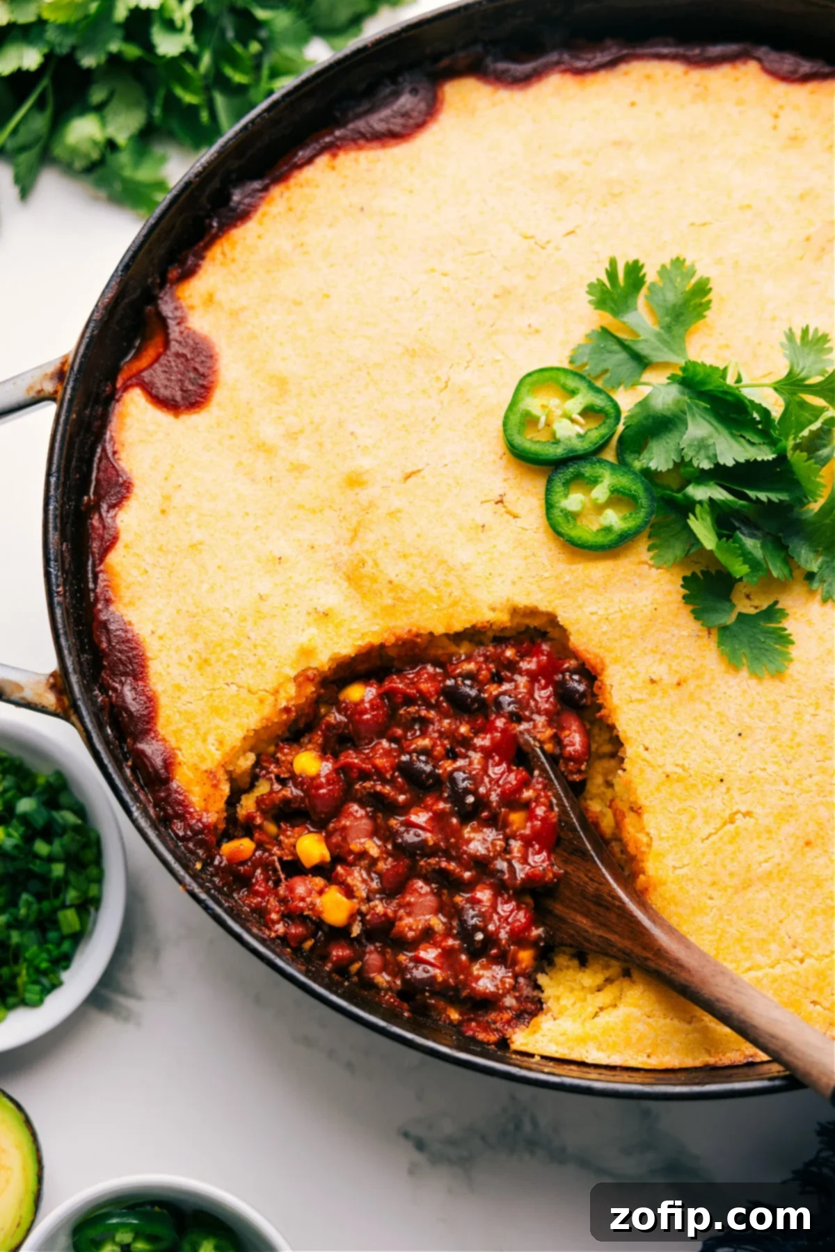 A large skillet filled with freshly baked cornbread casserole, showing a generous scoop being lifted, revealing the rich chili underneath its golden, fluffy cornbread crust. Perfect for serving.