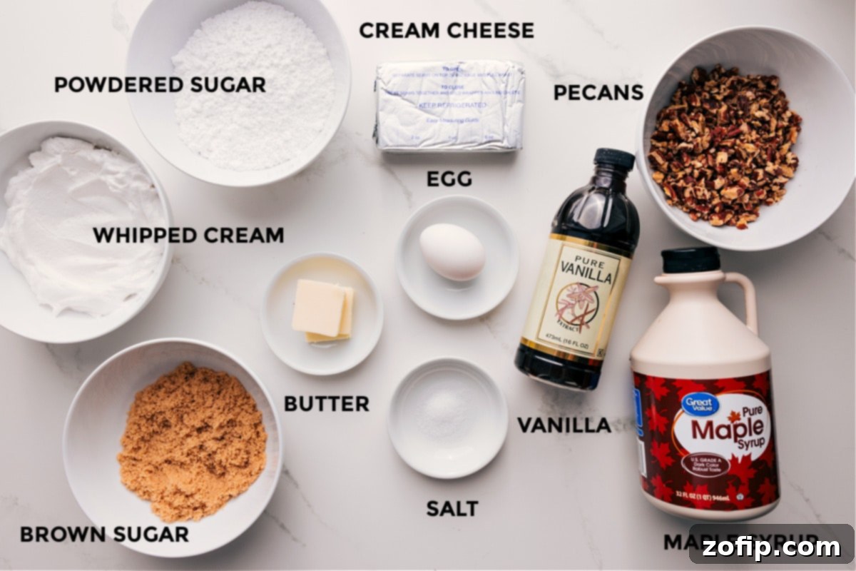 All the essential ingredients for Pecan Pie Dip artfully arranged on a counter, including cream cheese, whipped topping, powdered sugar, brown sugar, butter, maple syrup, pecans, egg, vanilla extract, and salt.