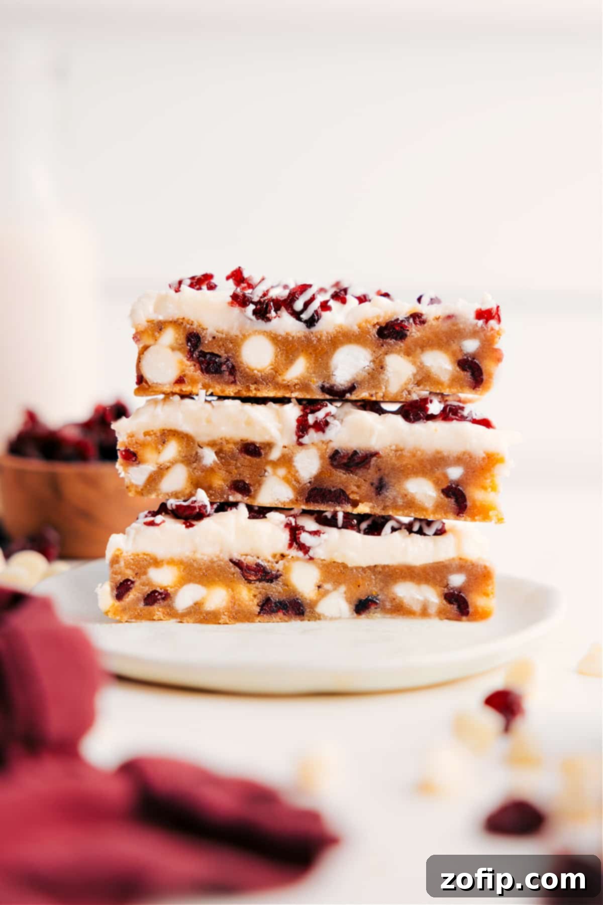 Cranberry Bliss Bars stacked on top of each other showing the layers of cranberries and white chocolate chips and frosting.