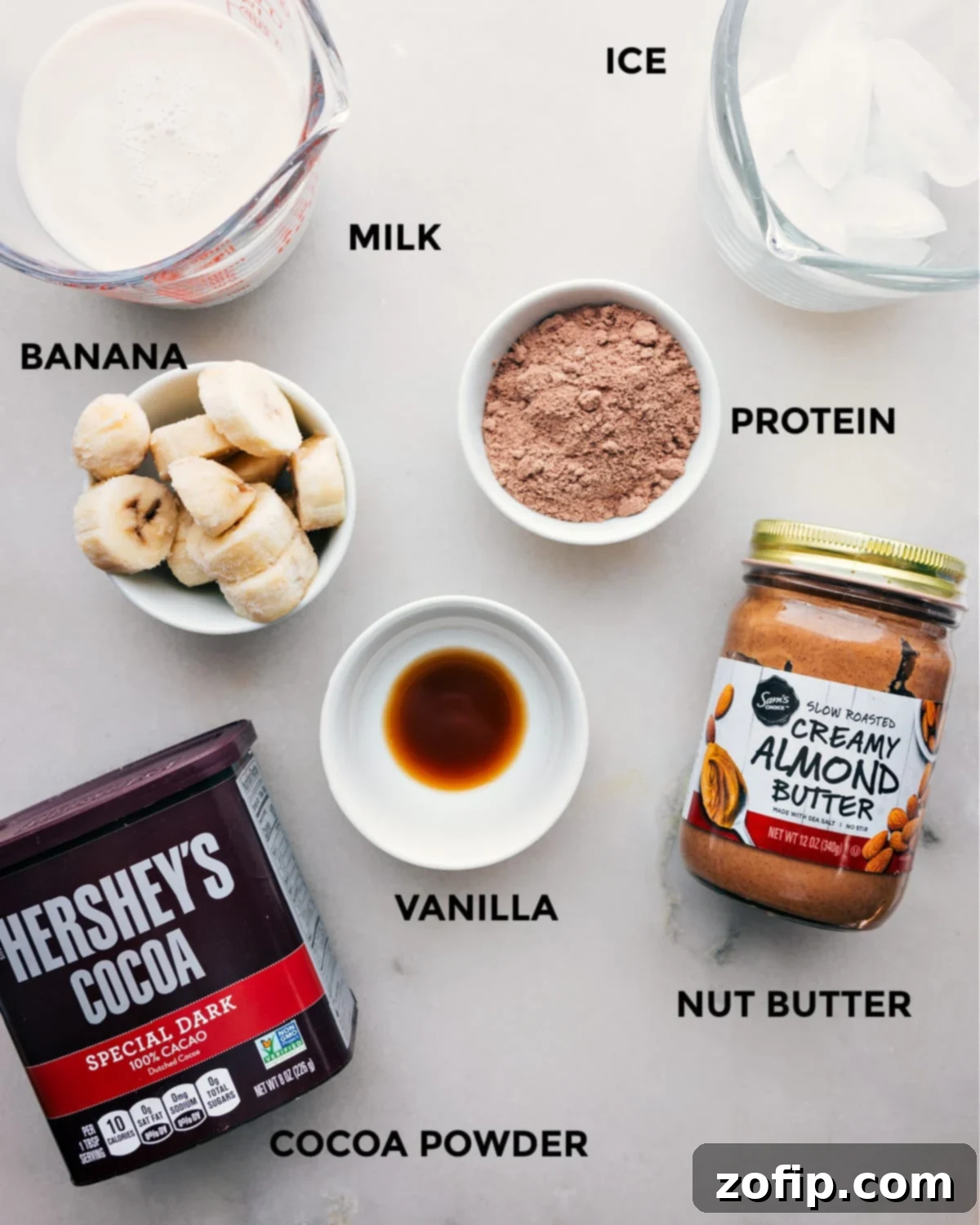 All the ingredients including milk, ice, cocoa powder, nut butter, vanilla, and protein powder prepped out for easy assembly.