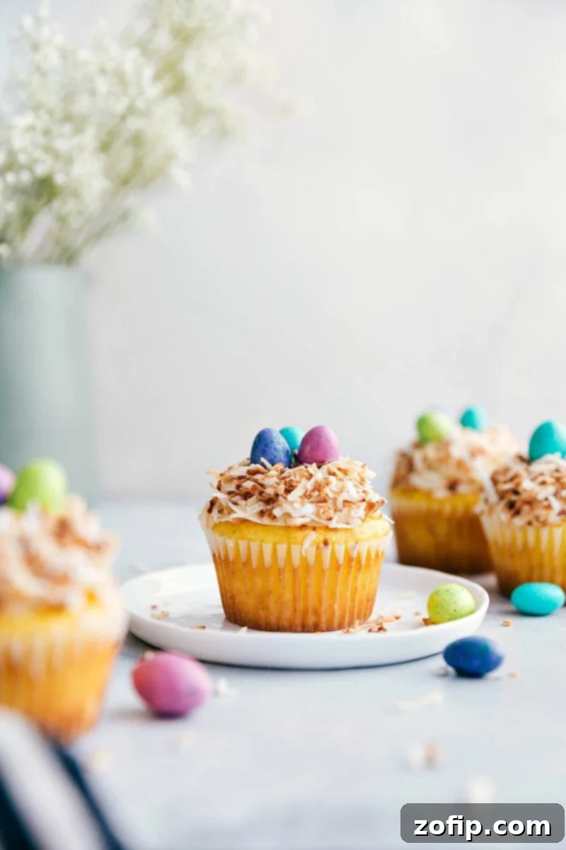 Delicious yellow cupcakes topped with the best cream cheese frosting, crunchy toasted coconut, and colorful M&M's, creating adorable bird's nest Easter treats. So simple and fun to make! Close-up of four bird's nest Easter cupcakes with speckled egg M&Ms and toasted coconut frosting