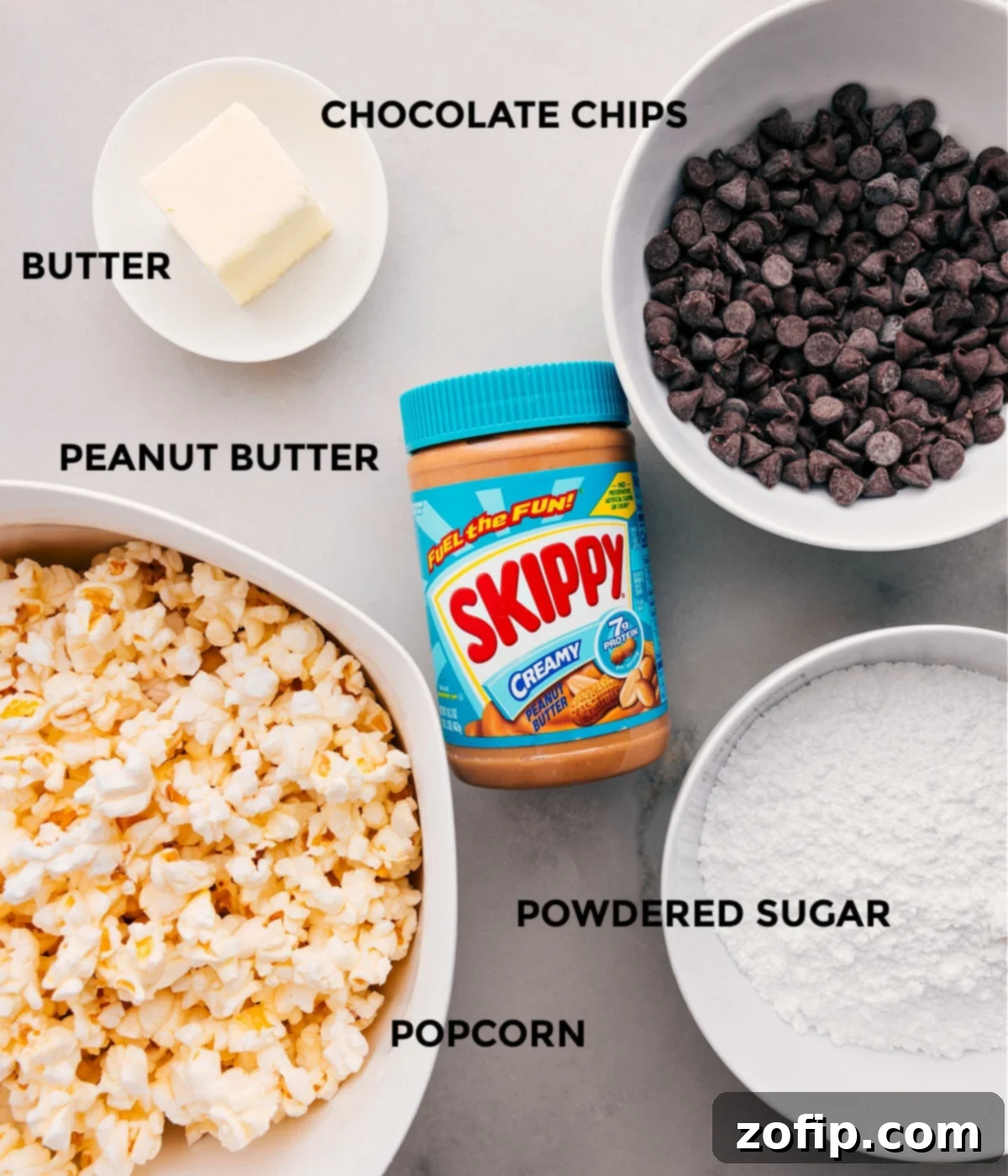 All the essential ingredients for Popcorn Puppy Chow laid out: fluffy popcorn, creamy peanut butter, rich chocolate chips, unsalted butter, a pinch of salt, and a generous amount of powdered sugar.