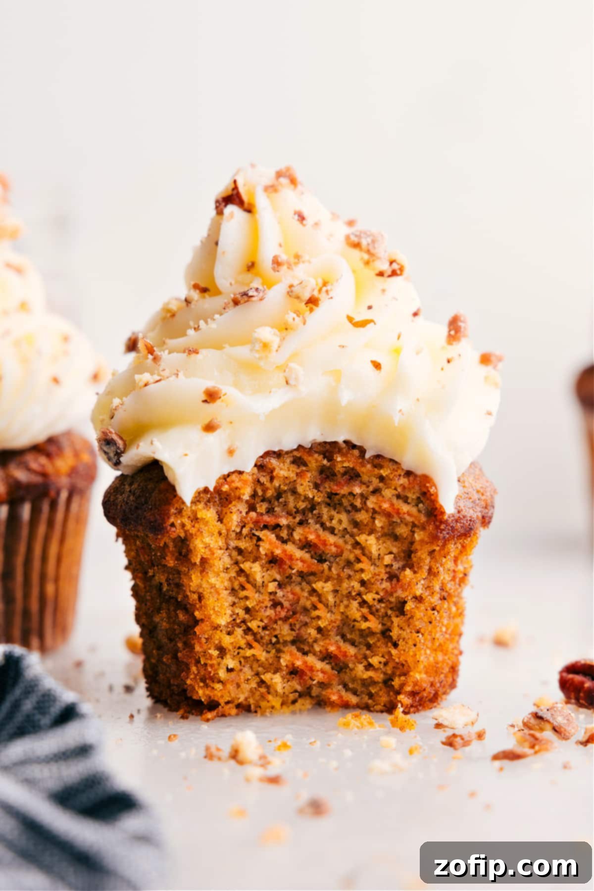A close-up of a carrot cake muffin with a generous bite taken out, revealing its moist interior and creamy frosting.