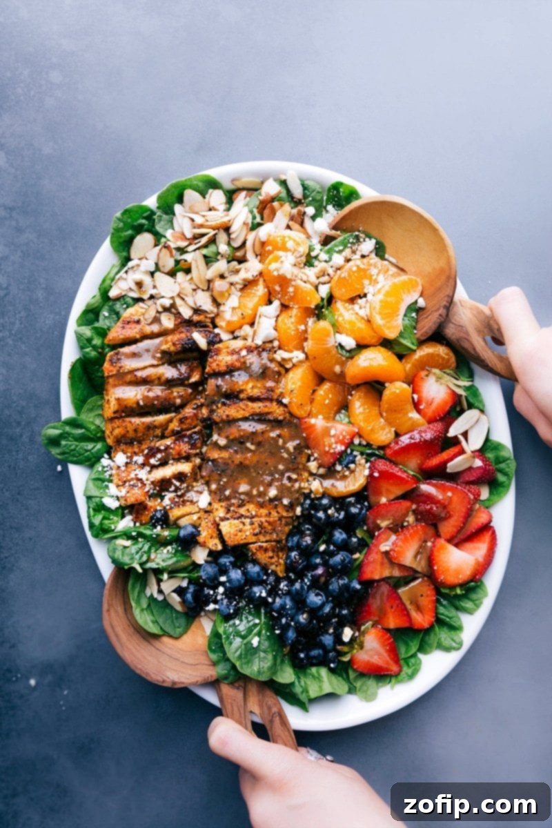 Elegant Chicken Spinach Salad Presentation: Freshly Dressed with Fruit and Nut Toppings A large platter showcasing a beautifully arranged Chicken Spinach Salad, garnished with fresh fruit and nuts, drizzled with dressing.