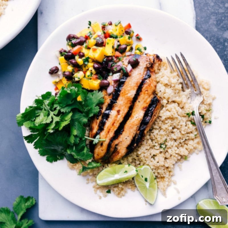 A delightful chicken quinoa bowl with mango salsa and rice, garnished with cilantro, ready to be enjoyed.