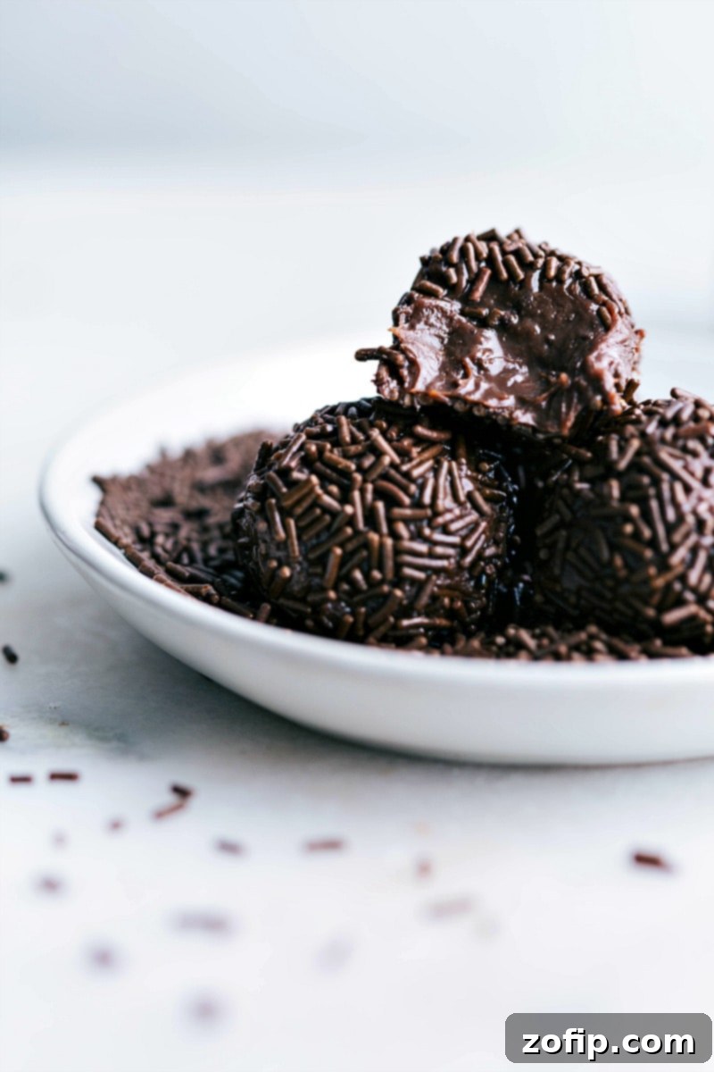 A delicious Brigadeiro, showcasing its rich, chewy texture. Brigadeiros with a bite out of one of them, revealing the fudgy interior.