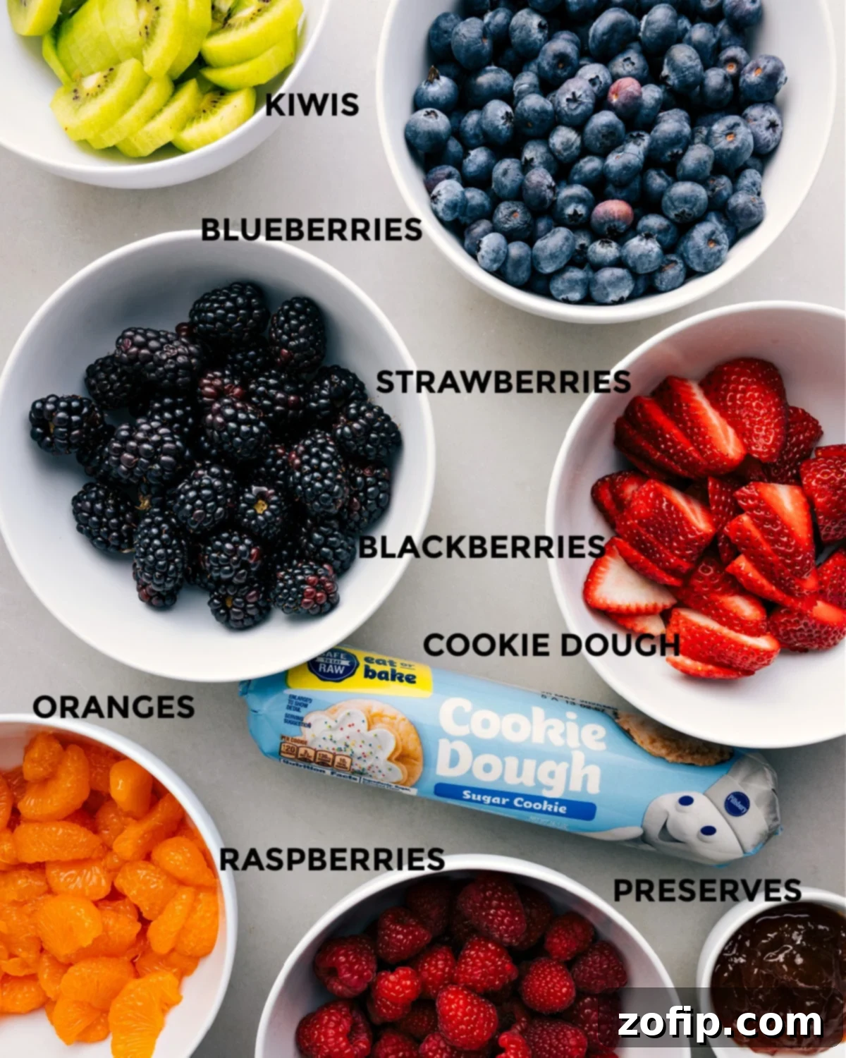 Ingredients for the Best Fruit Pizza Recipe Ingredients prepped for an easy fruit pizza assembly: fresh fruit, sugar cookie dough, and fruit preserves for the glaze.