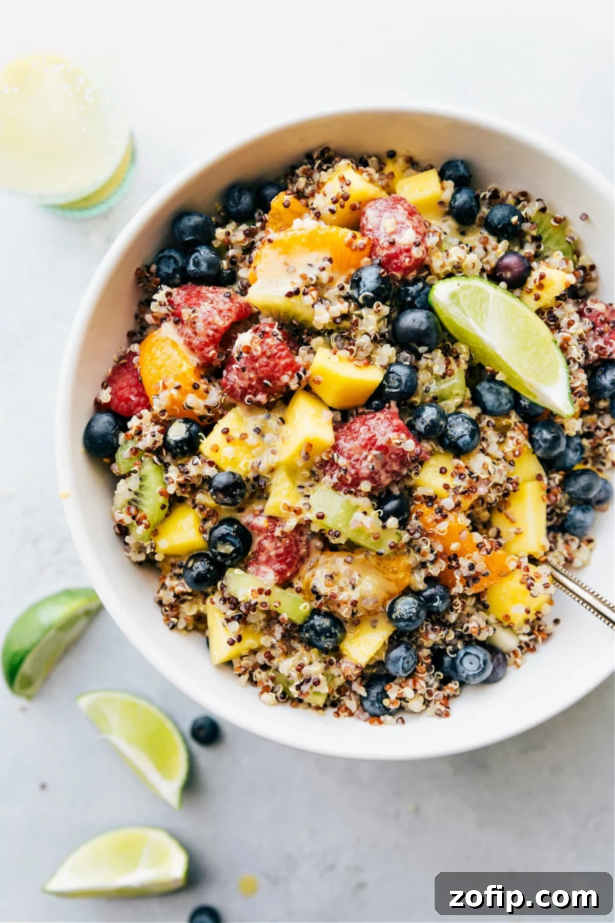 A vibrant bowl of Quinoa Fruit Salad, featuring colorful fresh fruits like mango, raspberries, kiwis, clementines, and blueberries mixed with fluffy tri-color quinoa, ready to be served.