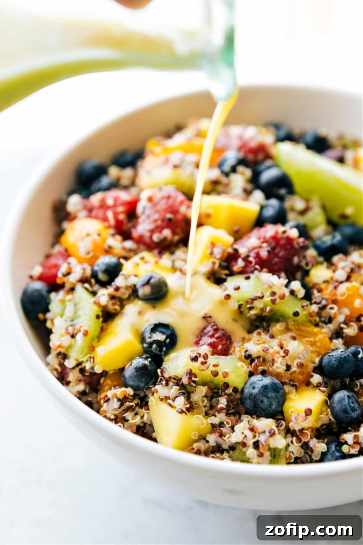 Our favorite Quinoa Fruit Salad, beautifully presented in a bowl, with the zesty citrus dressing being drizzled generously over the top just before serving.