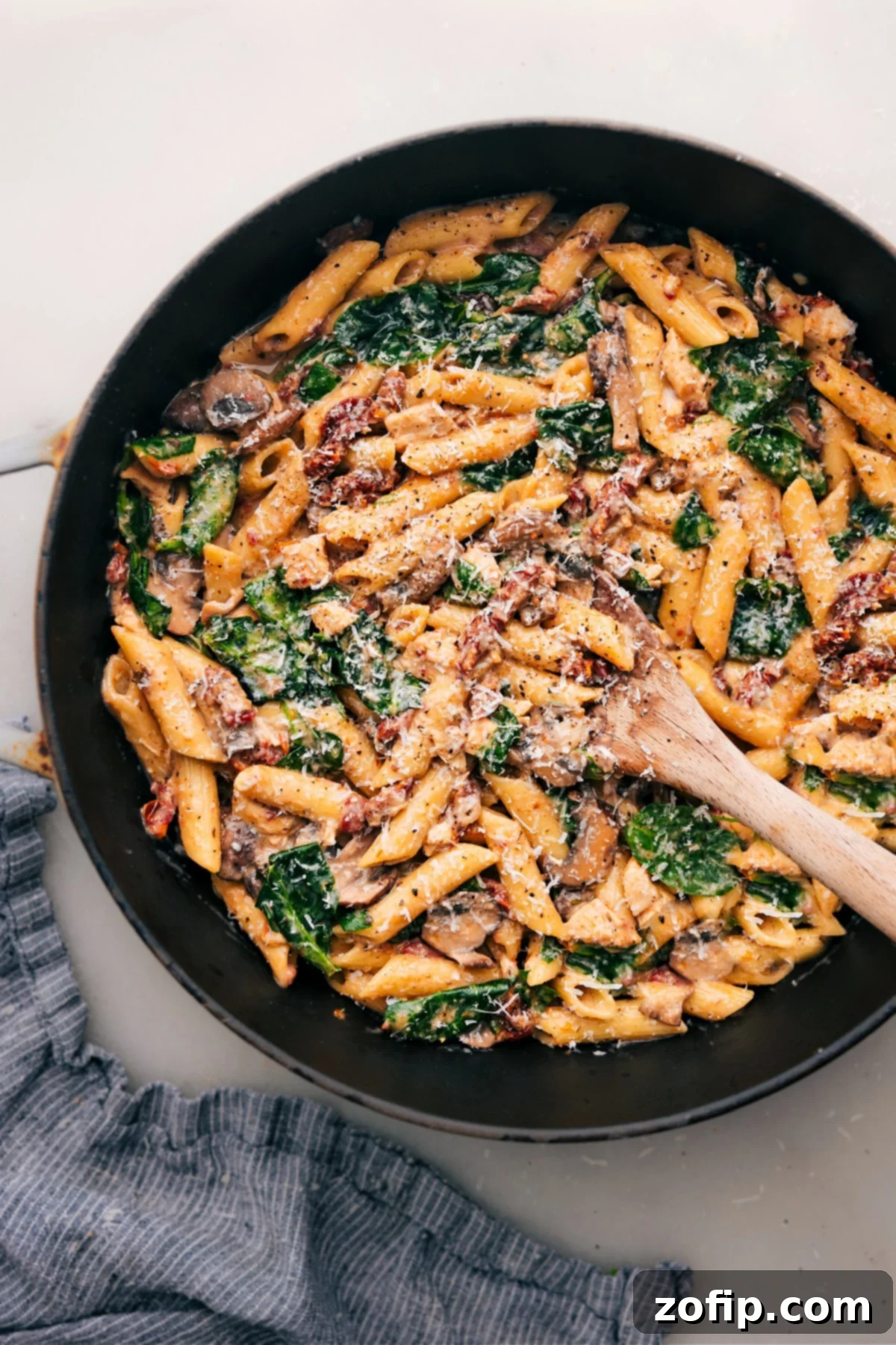 Warm Chicken Penne Pasta with Cheese, Sun-Dried Tomatoes, and Spinach A pot of warm chicken penne pasta features melted cheese, sun-dried tomatoes, and fresh spinach, ready to be served.