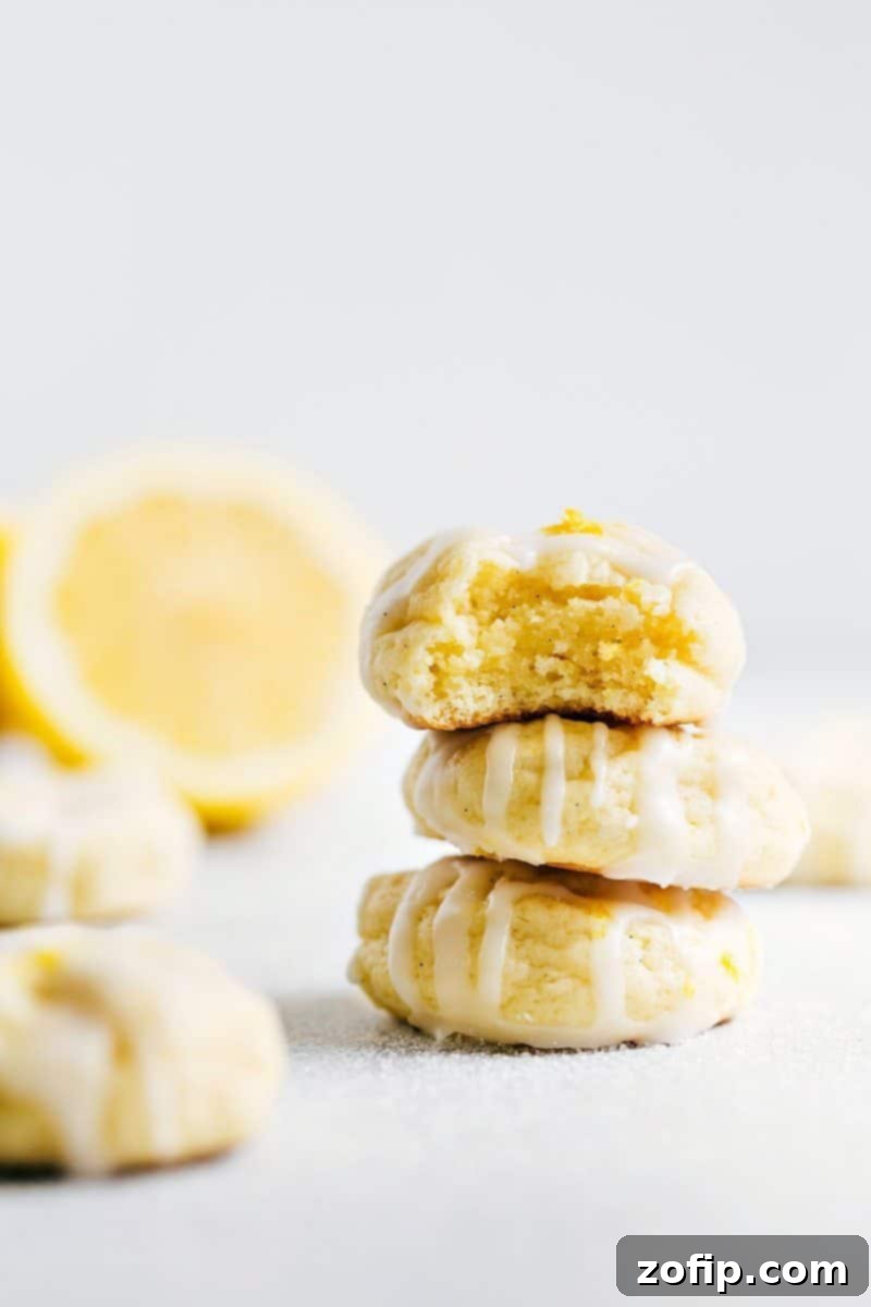 A stack of three lemon cheesecake cookies topped with a delicious frosting with a bite taken from the top cookie, showcasing its soft, chewy texture.