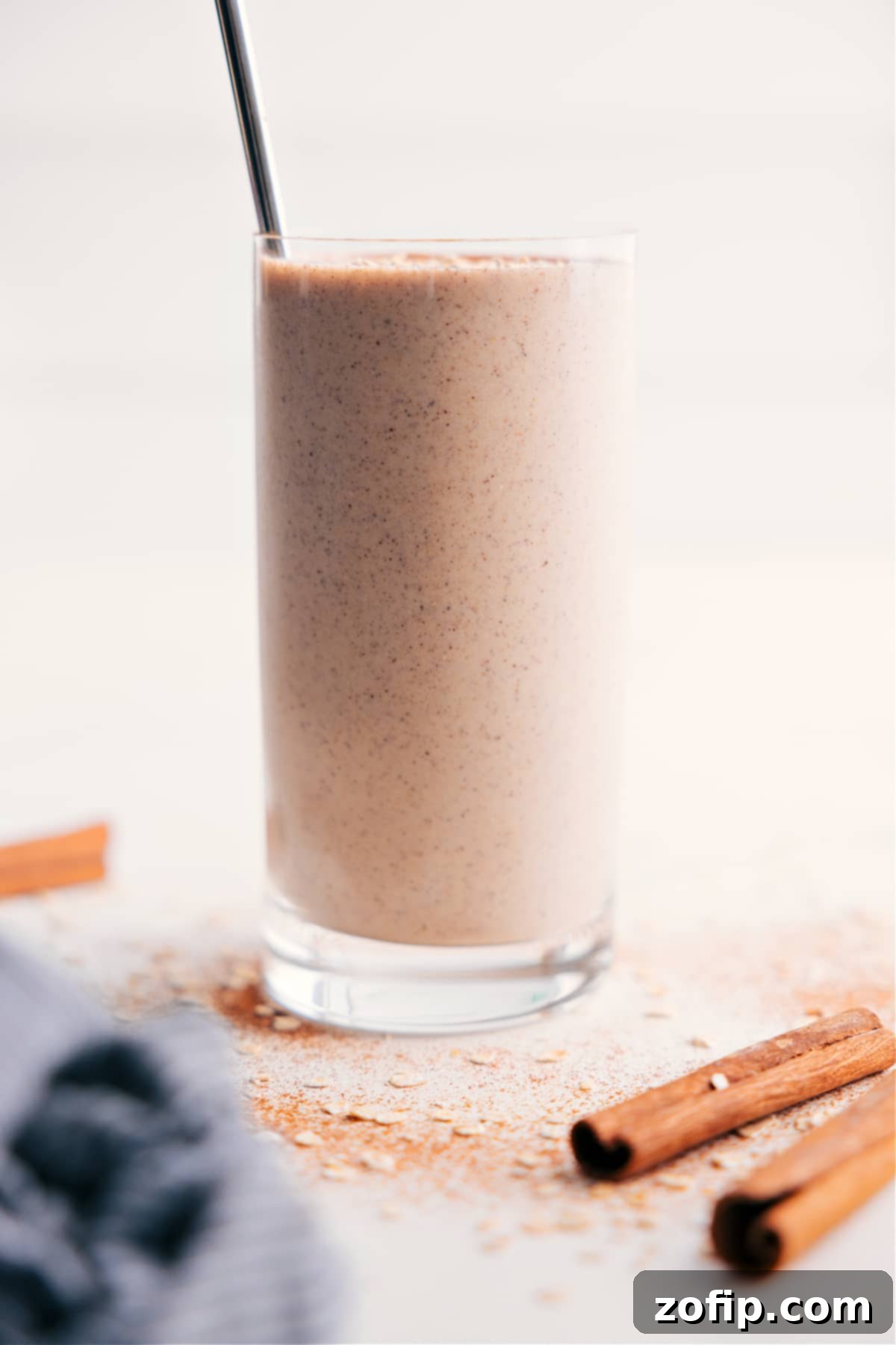 Creamy oatmeal smoothie in a glass with a straw, garnished with a sprinkle of cinnamon and a few whole oats.