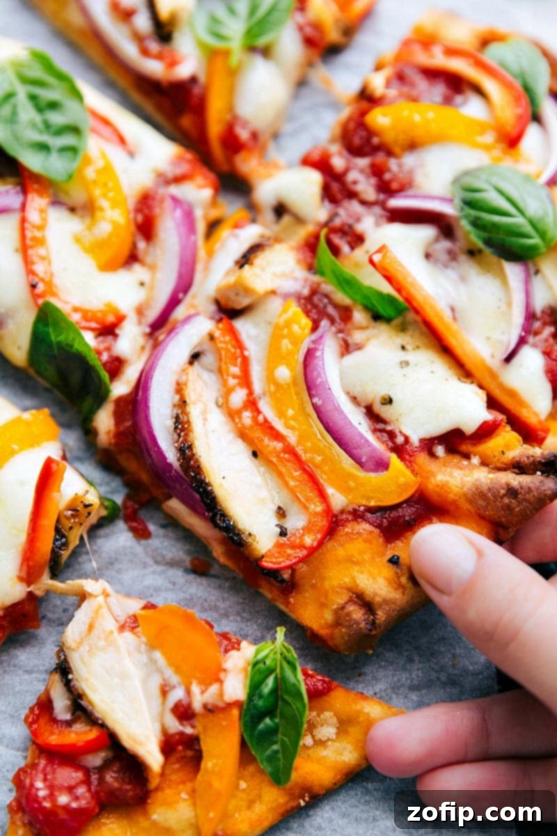Freshly baked flatbread pizza with melted cheese, vibrant vegetables, and a golden crust, with a slice being pulled away, showcasing its delicious texture.