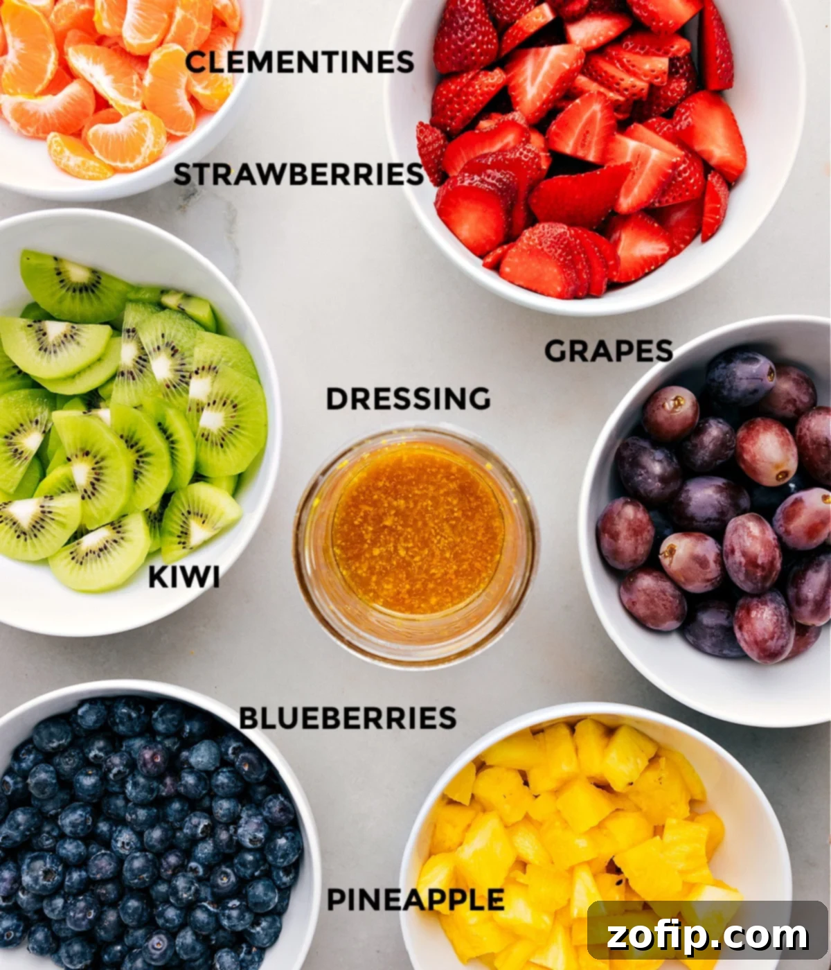 How To Make Fruit Salad - Prepped Ingredients All the fresh fruit salad ingredients, including pineapple, strawberries, kiwi, grapes, clementines, and blueberries, prepped and ready for assembly.