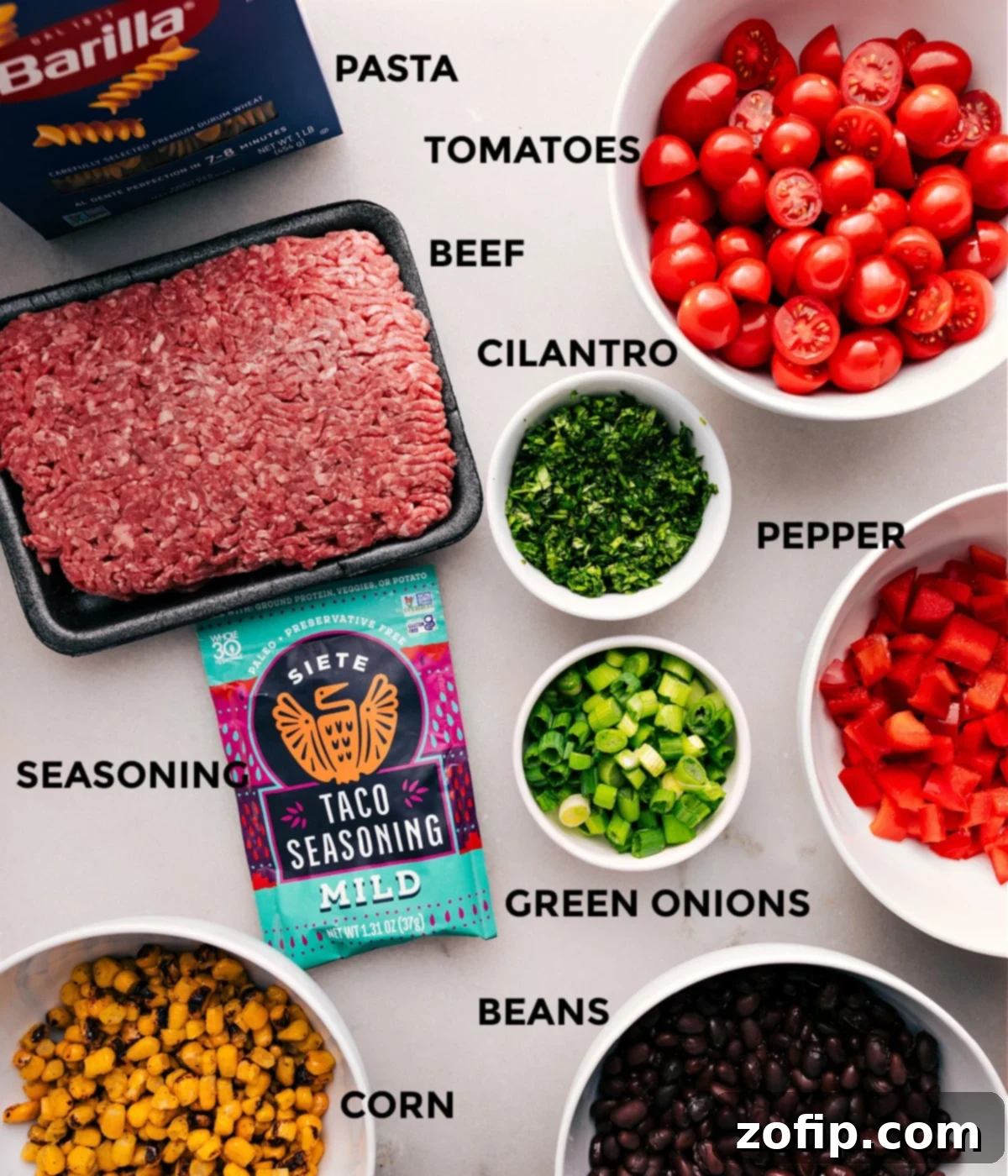 All the fresh ingredients for Taco Pasta Salad, including cooked pasta, seasoned ground beef, vibrant red bell pepper, cherry tomatoes, green onions, cilantro, black beans, and corn, laid out on a clean surface, ready for assembly.