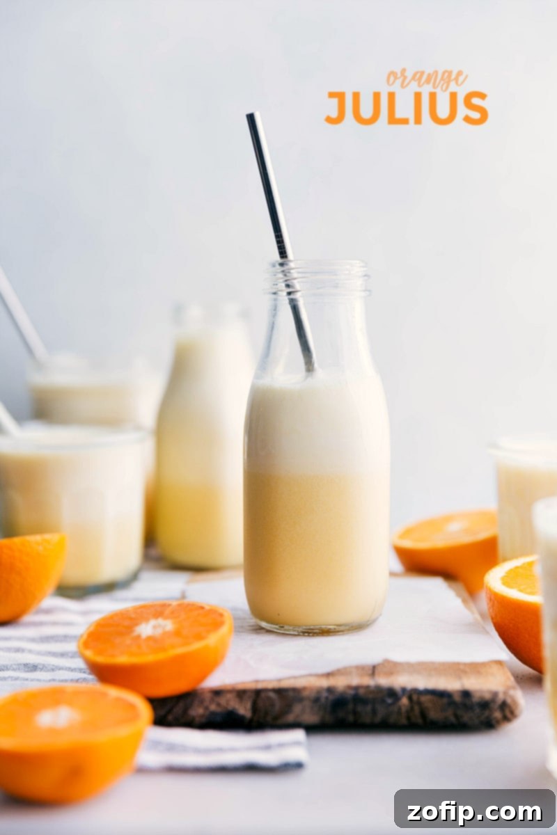 Two glasses of frothy Orange Julius with fresh orange slices on the side, ready to be enjoyed.