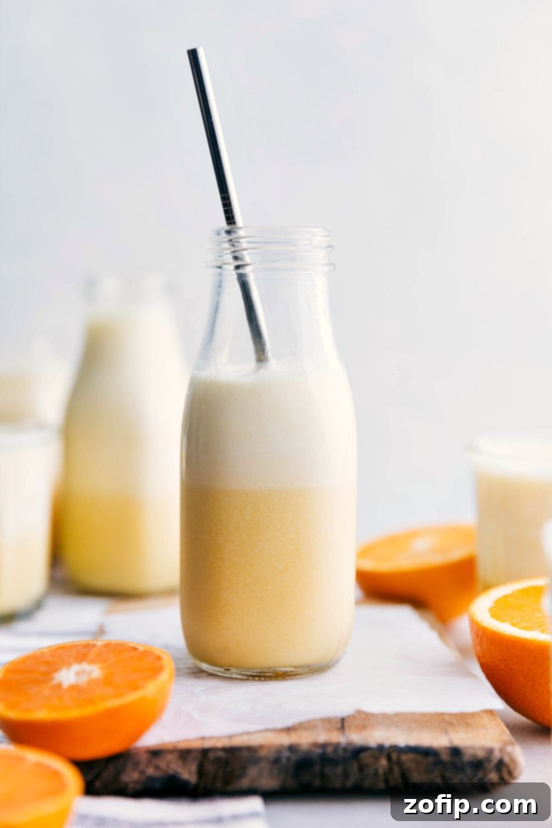 A glass of ready-to-drink Orange Julius with a straw, garnished with an orange slice, surrounded by cut oranges.