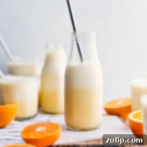 A tall glass of Orange Julius with a straw and orange slice garnish.